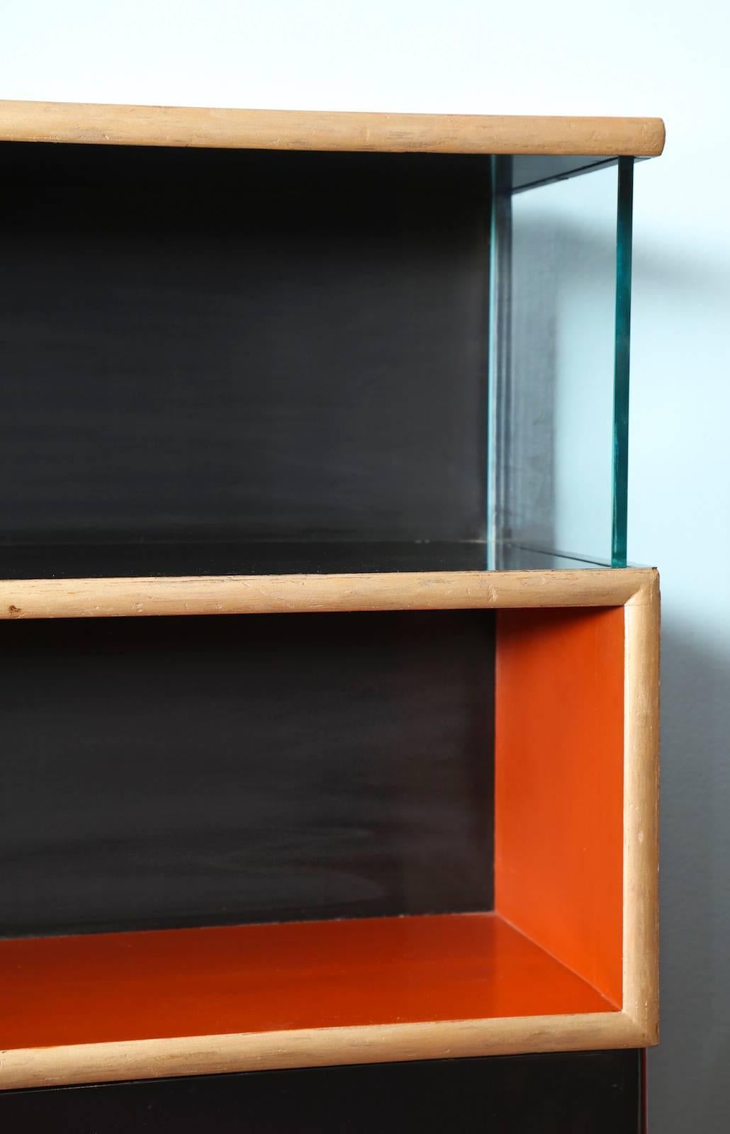 Seltener, von Paul Frankl entworfener Bücher- und Aufbewahrungsschrank. Orange und schwarz lackiertes Holz, mit goldfarbener Oberfläche in einem sich schlängelnden geometrischen Motiv und dicken Glas-Seitenteilen. Ein seltenes Beispiel für
