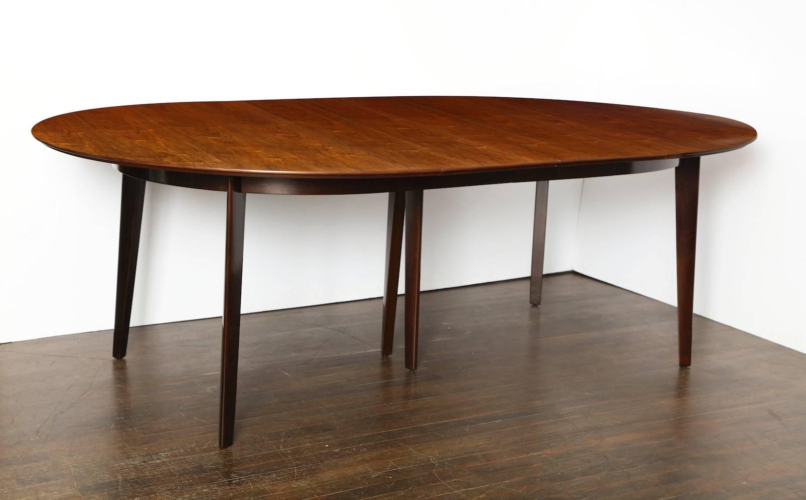 Edward Wormley Expandable Dining Table #696, for Dunbar.  Slightly oval top of figured walnut, with dark stained mahogany legs and two leaves. Retractable center leg for support when the table is extended. Recently refinished and in excellent