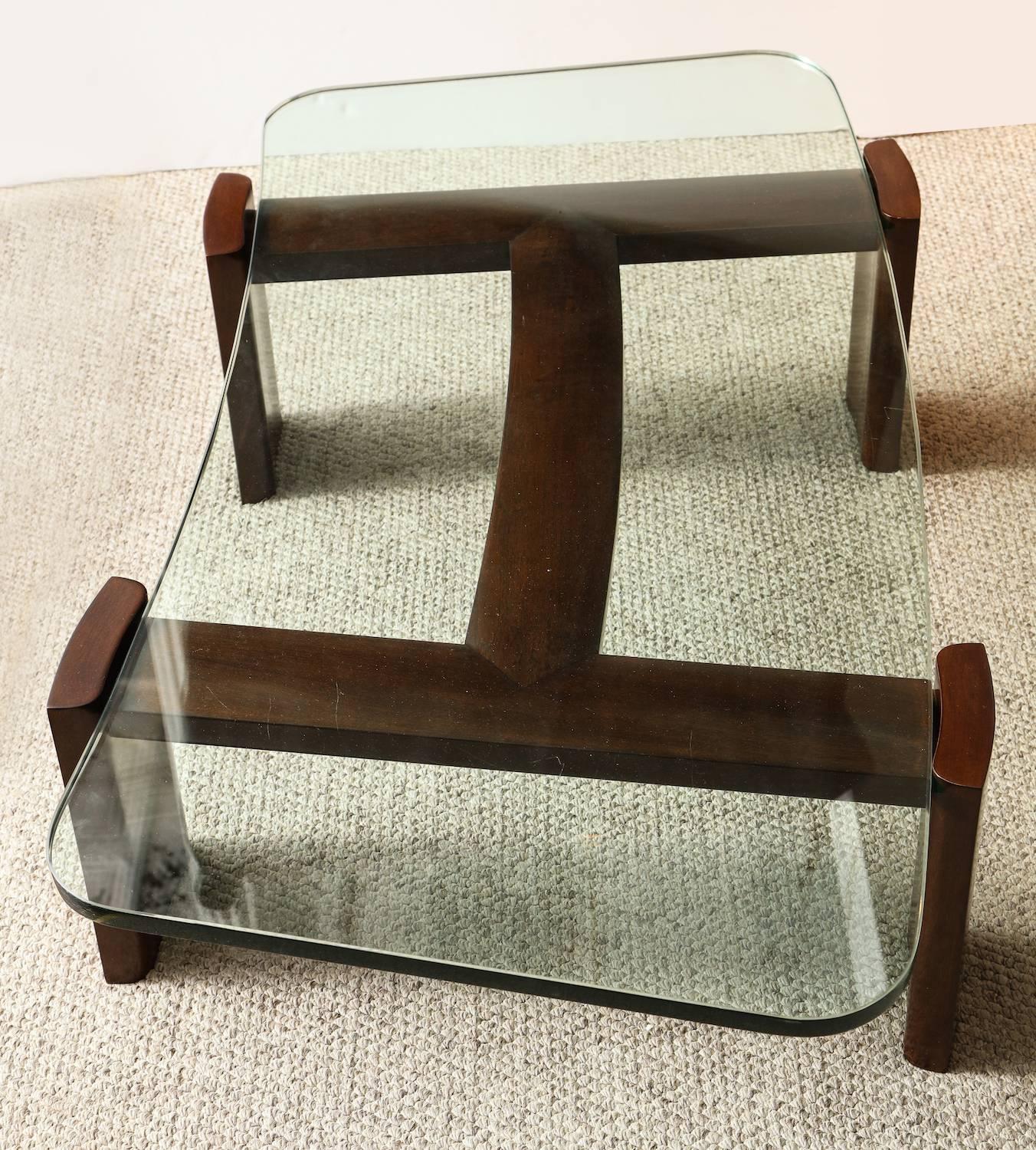 Paul Laszlo custom table of dark stained mahogany. Shaped elements joined to form and abstract "H" shape. Thick, curved glass top insets into the structure. Paul Laszlo metal label affixed to underside of table.