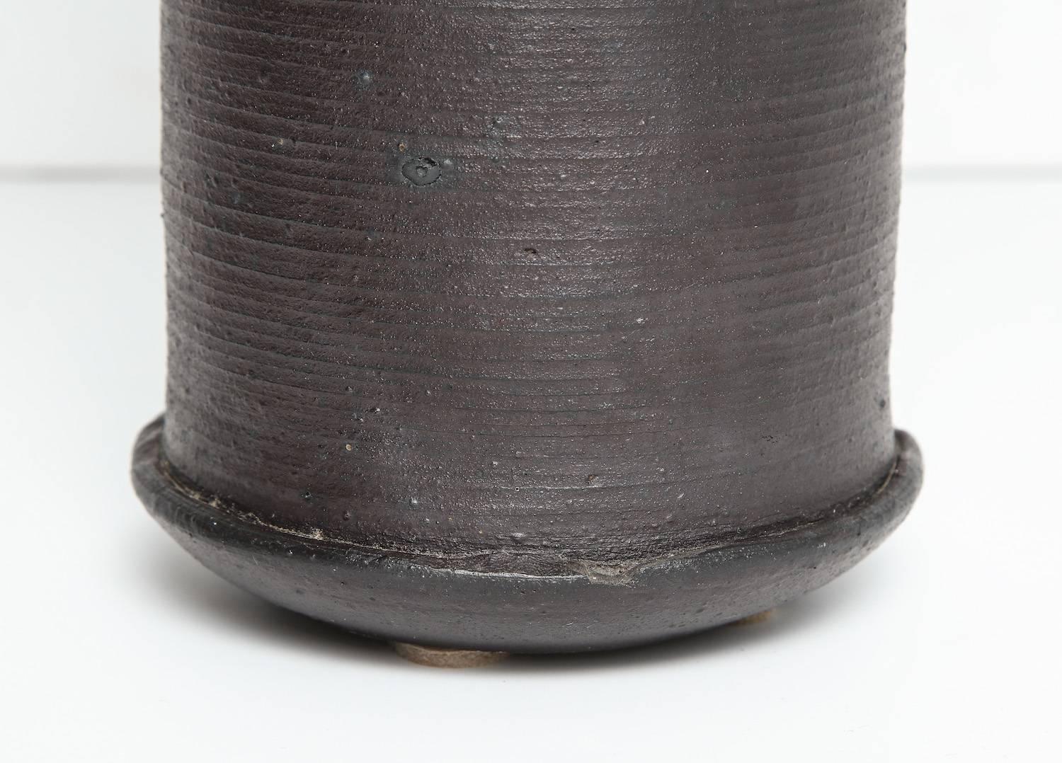 Cylindrical form with a curved bottom. Bottom half covered in dark brown matte glaze with incised horizontal lines. Top half running over with thick, cream colored glaze. Artist signed on the underside.