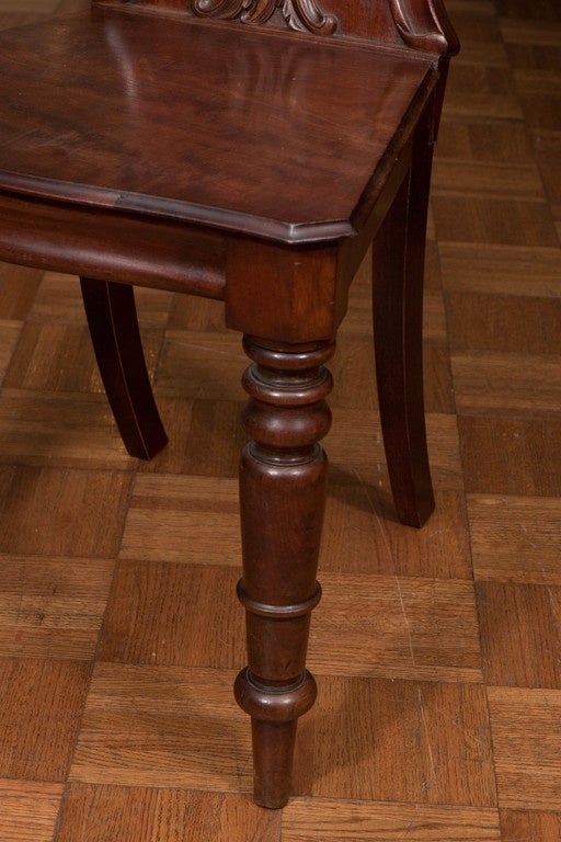 Four mahogany hall chairs on turned legs with crest carving on the backs.