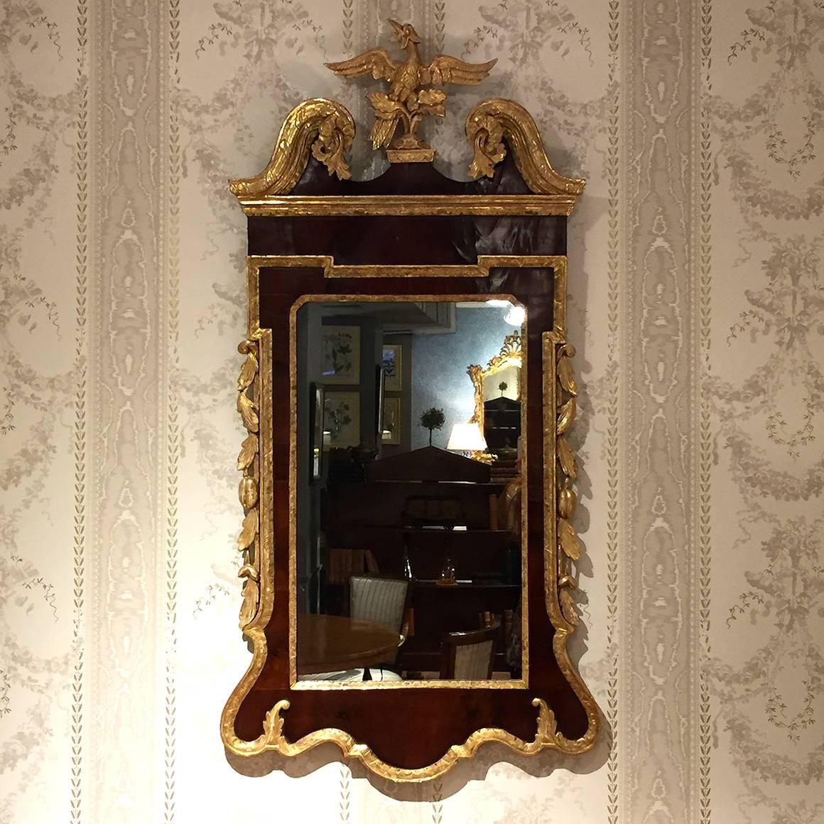 This George II mahogany and parcel gilt mirror is topped by a swan's neck pediment which is centered by a gilt ho-ho bird. The sides are ornamented with gilt fruiting vinery, flanking a rectangular mirror glass, and above a shaped apron.