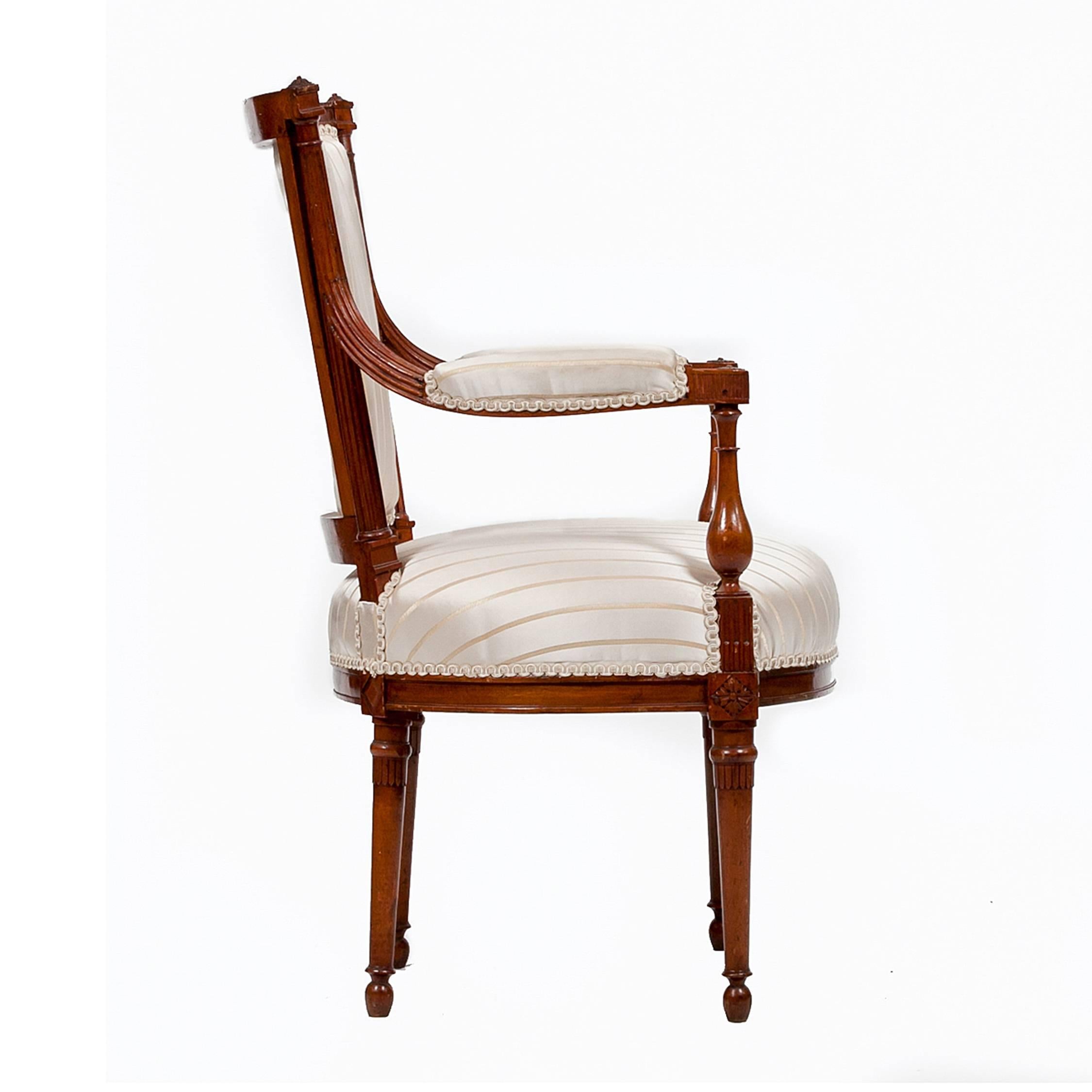 These delicately proportioned 18th-century fauteuil armchairs exemplify the French Directoire style, each with a barreled back, and rosette finials atop fluted stiles, that branch into padded armrests with baluster supports, which then extend into