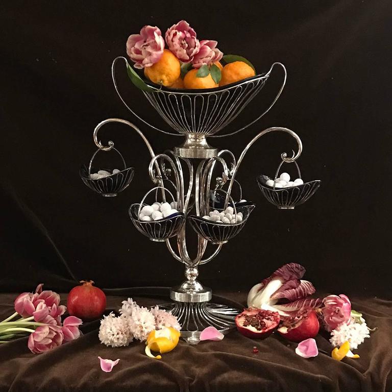 This English Sheffield plate wire-work epergne is distinguished by gracefully scrolled supports, which branch from a round footed base and suspend six baskets, with a large central basket at the top. Each of the baskets is shaped to hold a