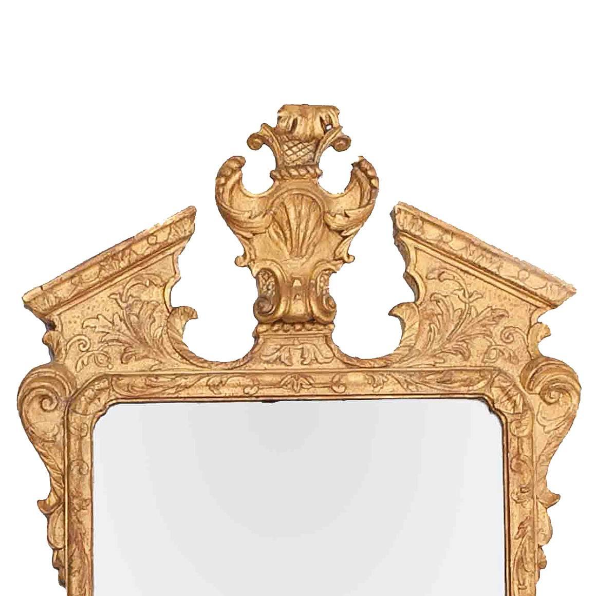 This early 18th century Irish George I wall mirror is topped by a broken pediment with a shell and acanthus leaf cartouche. The shaped apron is adorned with a scallop shell, and frame itself is ornamented with an acanthus leaf and strapwork motif.