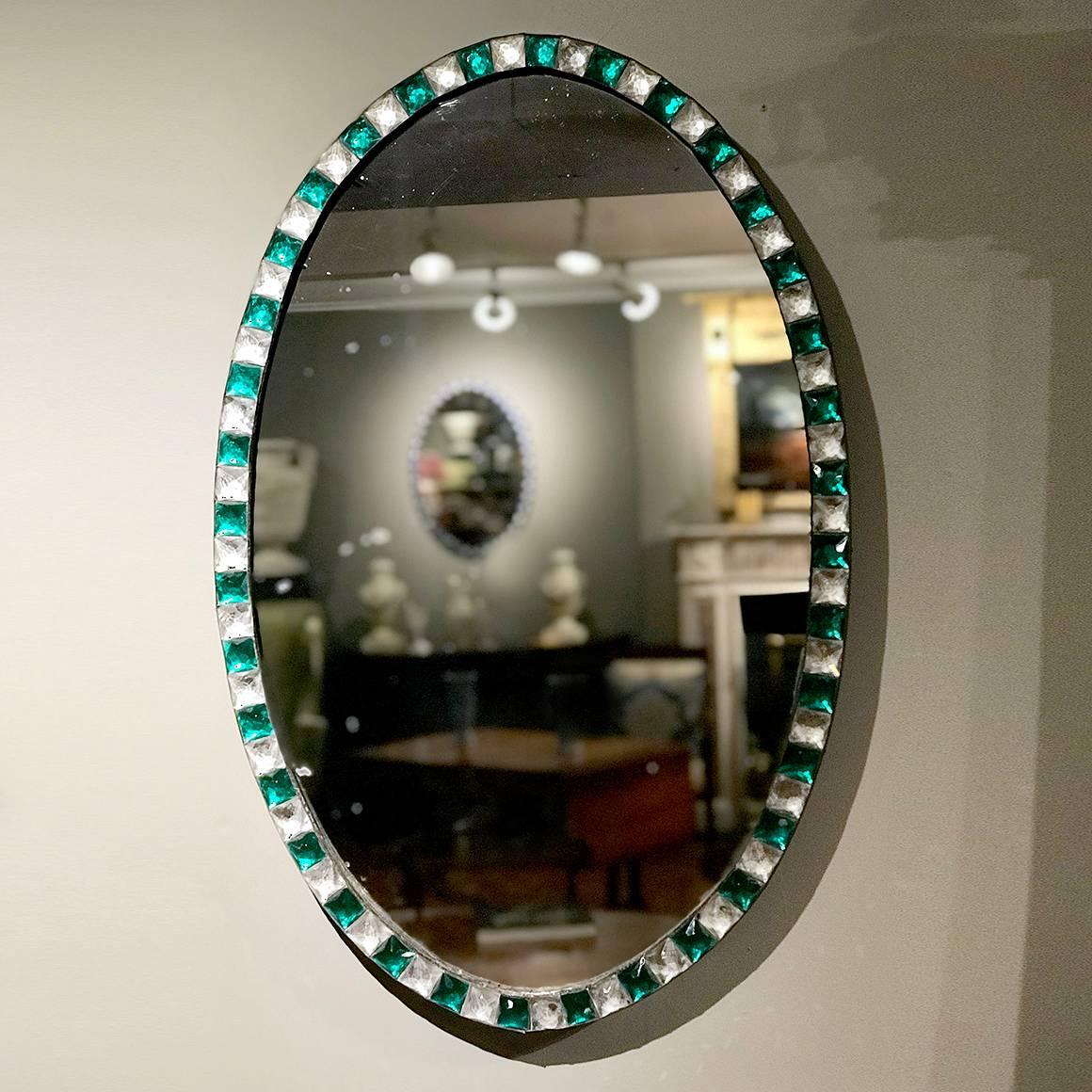 This distinctive Irish Georgian oval mirror is set apart by its unusual alternating green and clear faceted cut glass gems, set into a metal oval frame.