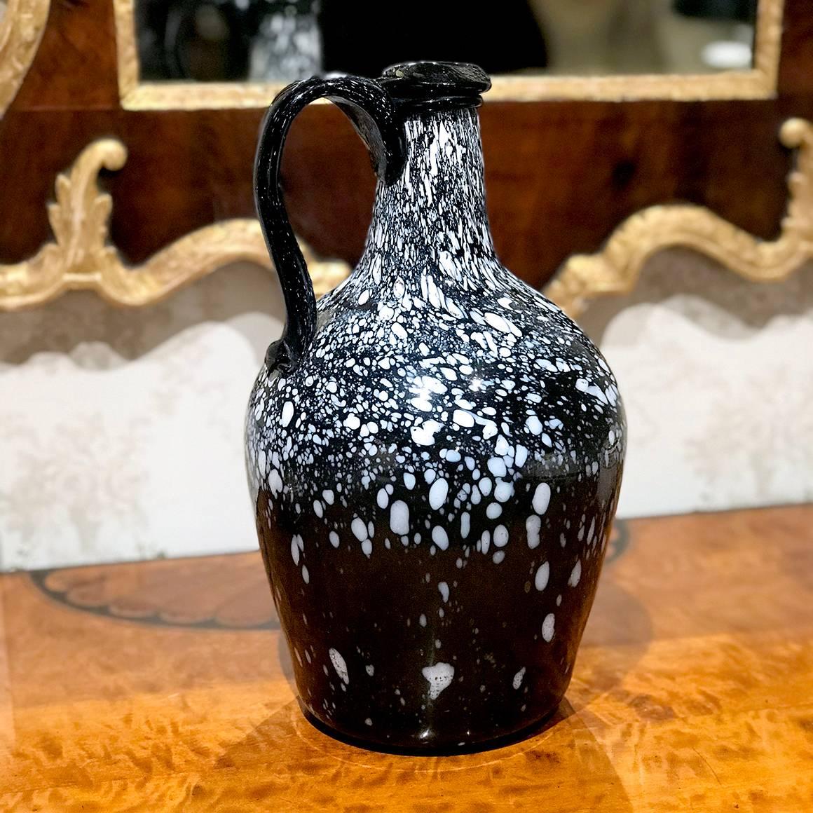 Nailsea Glassworks, in Somerset, England, was known for its distinctively colored and patterned pieces, which they produced from the late 18th century until the mid-19th century. This narrow-necked, handled glass jug is made from striking mottled