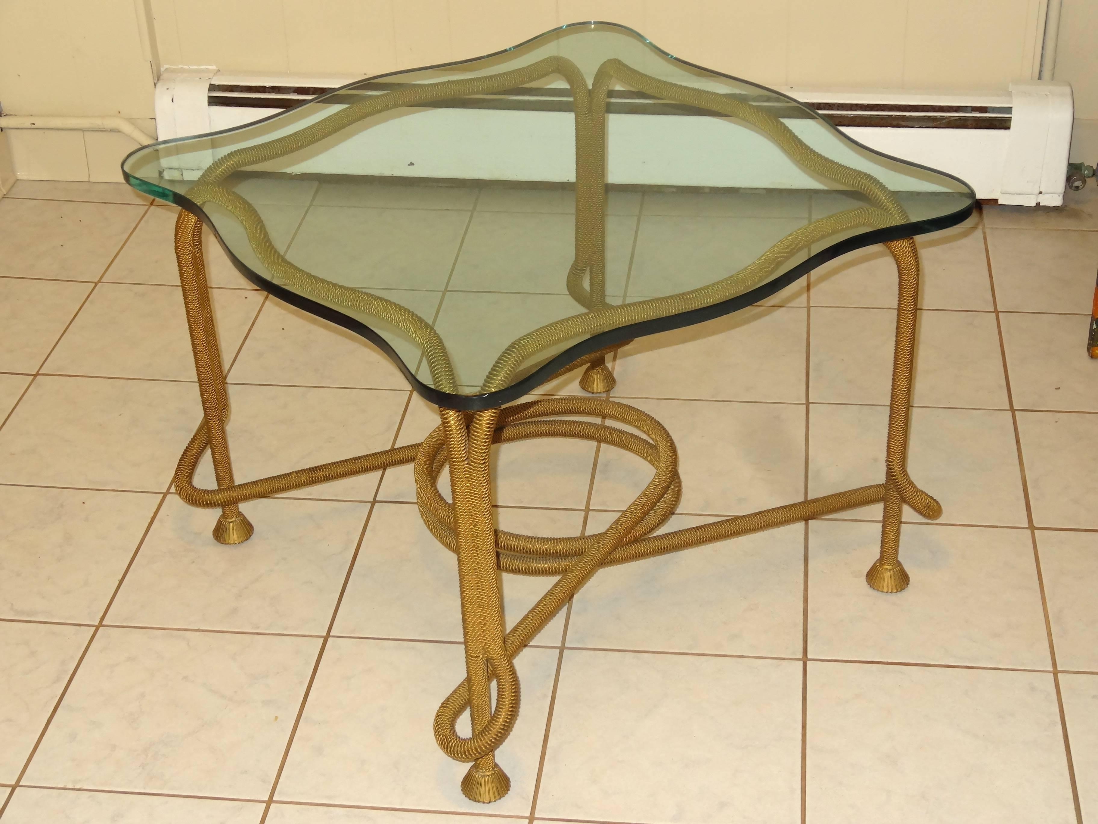French beaded rope table. Has metal frame that is covered with brass colored metal string to make it look like rope.
Nice whimsical shape and glass top that follows the form of the rope base.