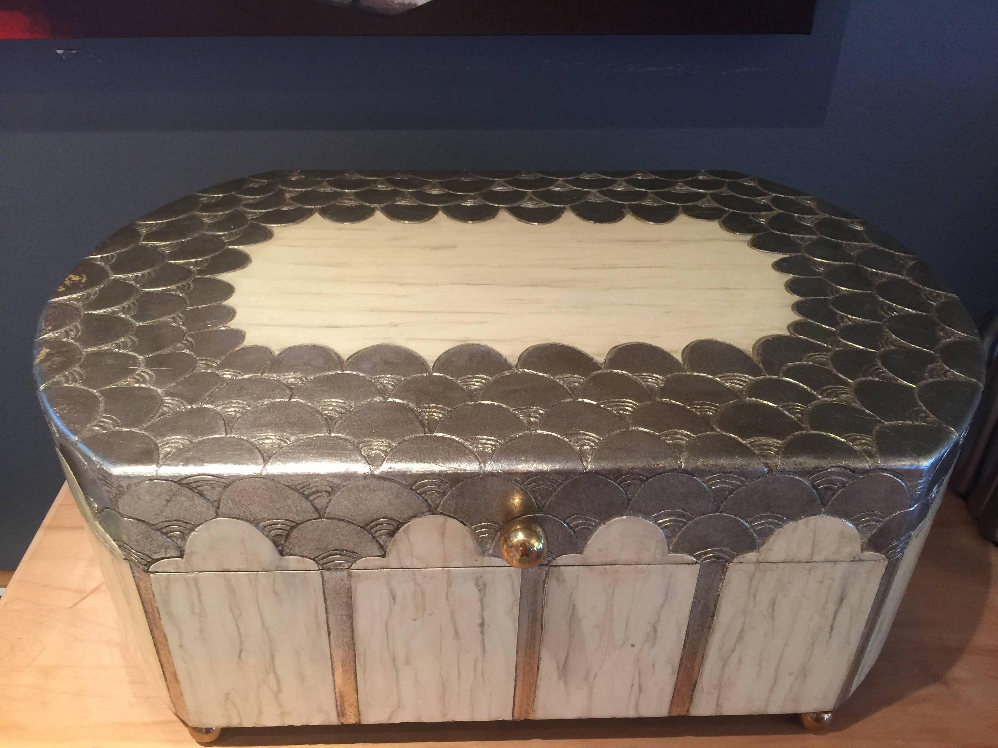 A beautifully detailed box in the deco style.
Designed with a silver leaf deco pattern which is complimented by what appears to be sliced bone.
the box rests on brass ball feet.
Great color combination and use of material.
Scaled beautifully.