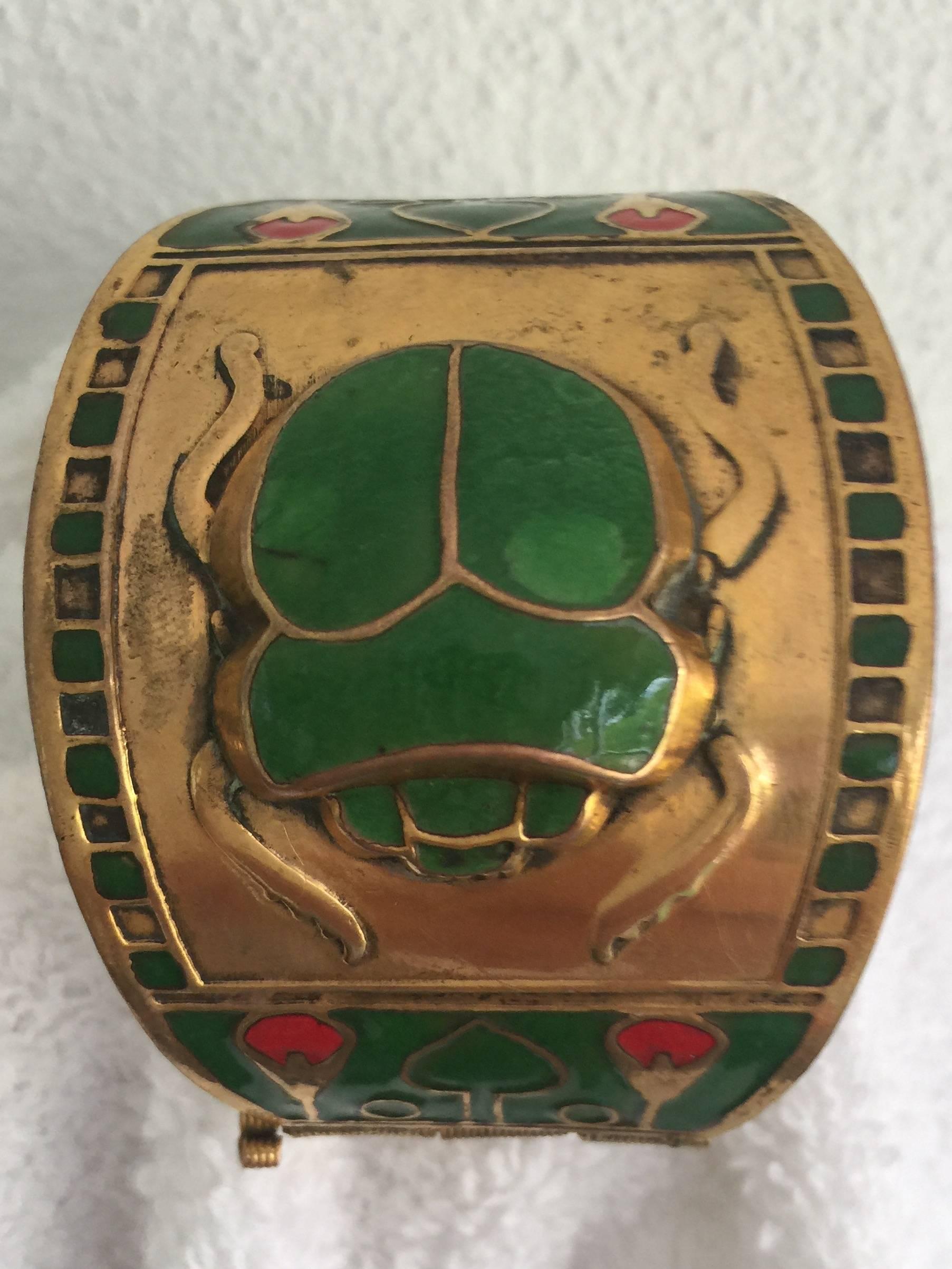 An Egyptian revival style cuff in enamel and brass. Beautifully designed with a scarab and lotus motif. 
The design is highlighted by the vibrant and complimentary colors.
Hinged with a pin closure.
Beautiful piece of jewlery.
Seems to have an