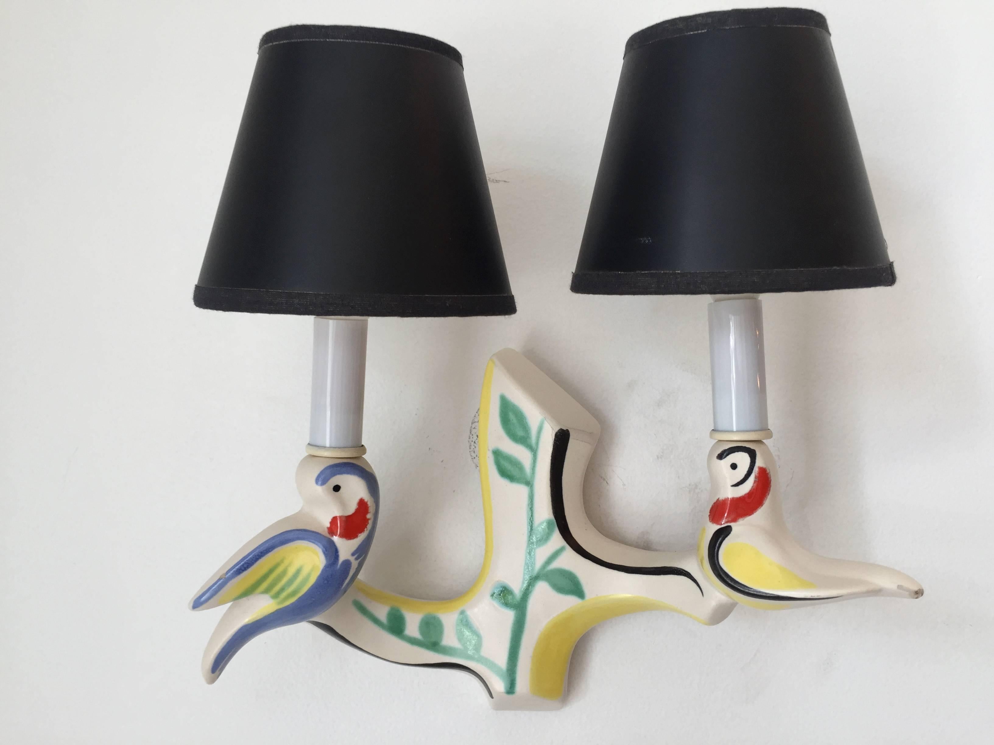 An original pair of French, 1950s handmade art pottery sconces composed of two birds holding two shades. Hand-painted and glazed.