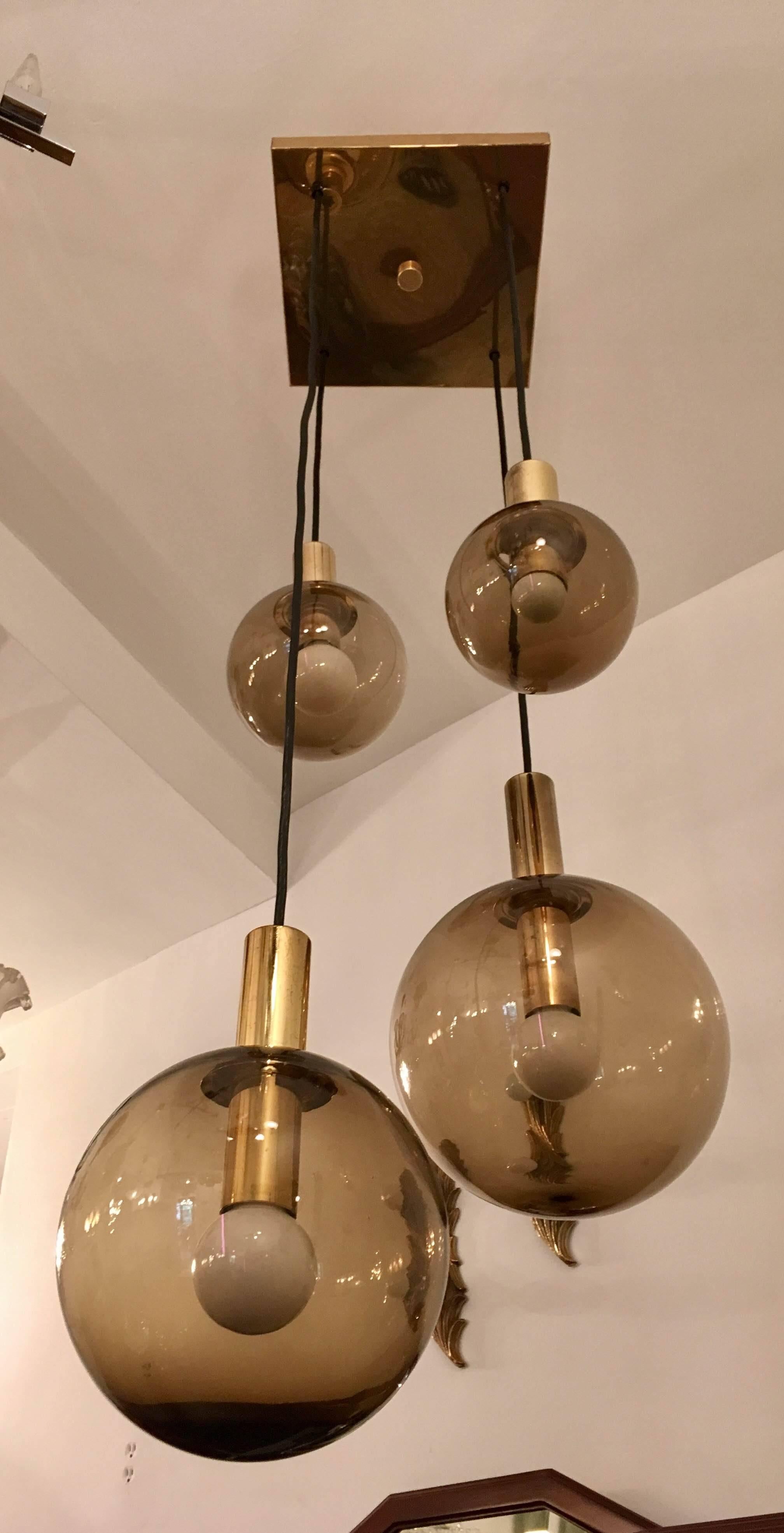A great original 1970 high style chandelier composed of a square polished brass fixture and four smoked glass globe shades. Made by RAAK.