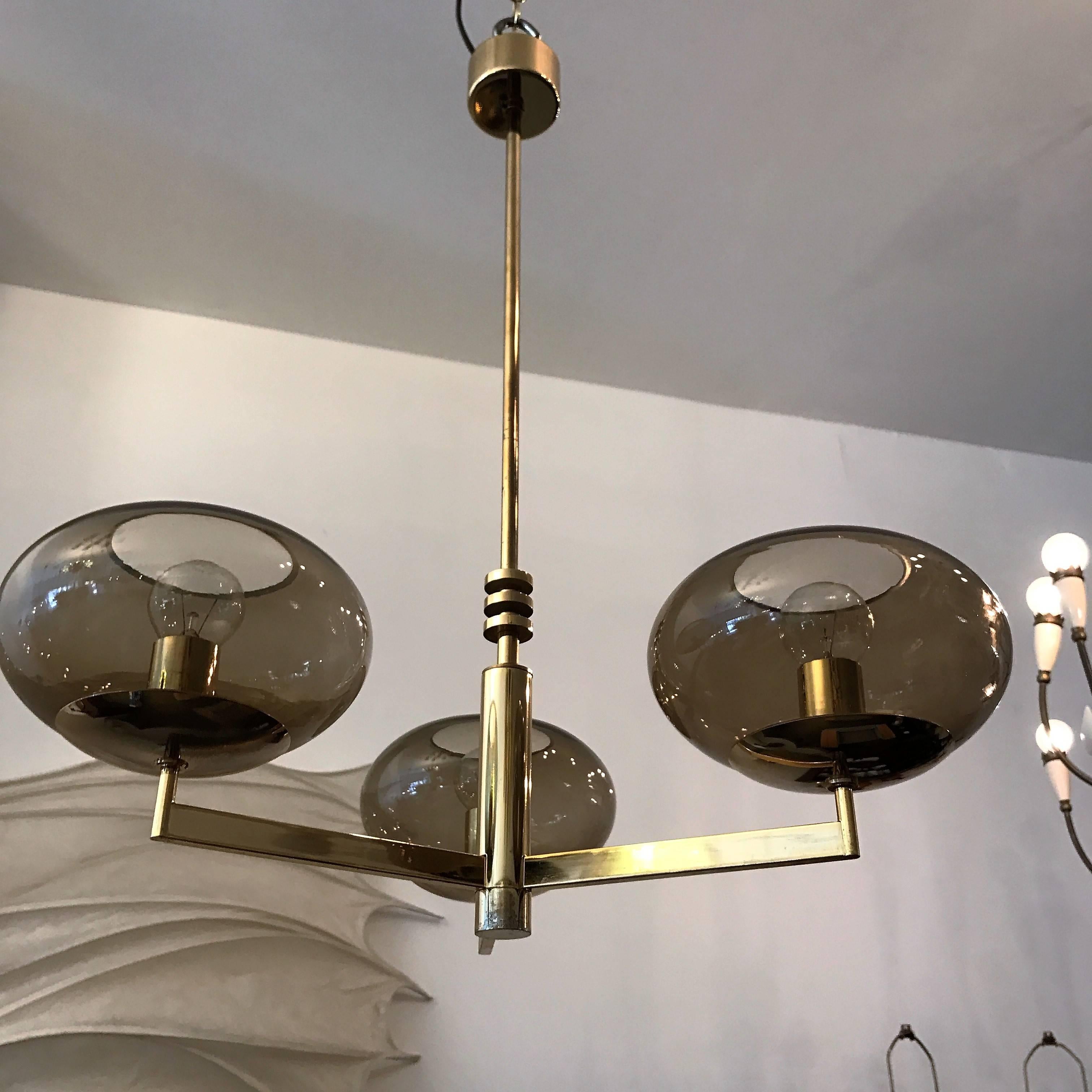 A sleek set of original 1970s modern three-arm pendants by the famed Italian lighting company, Sciolari. They are composed of polished brass fixtures and smoked glass globe shades, Newly rewired,  Matching sconces and larger chandeliers available.