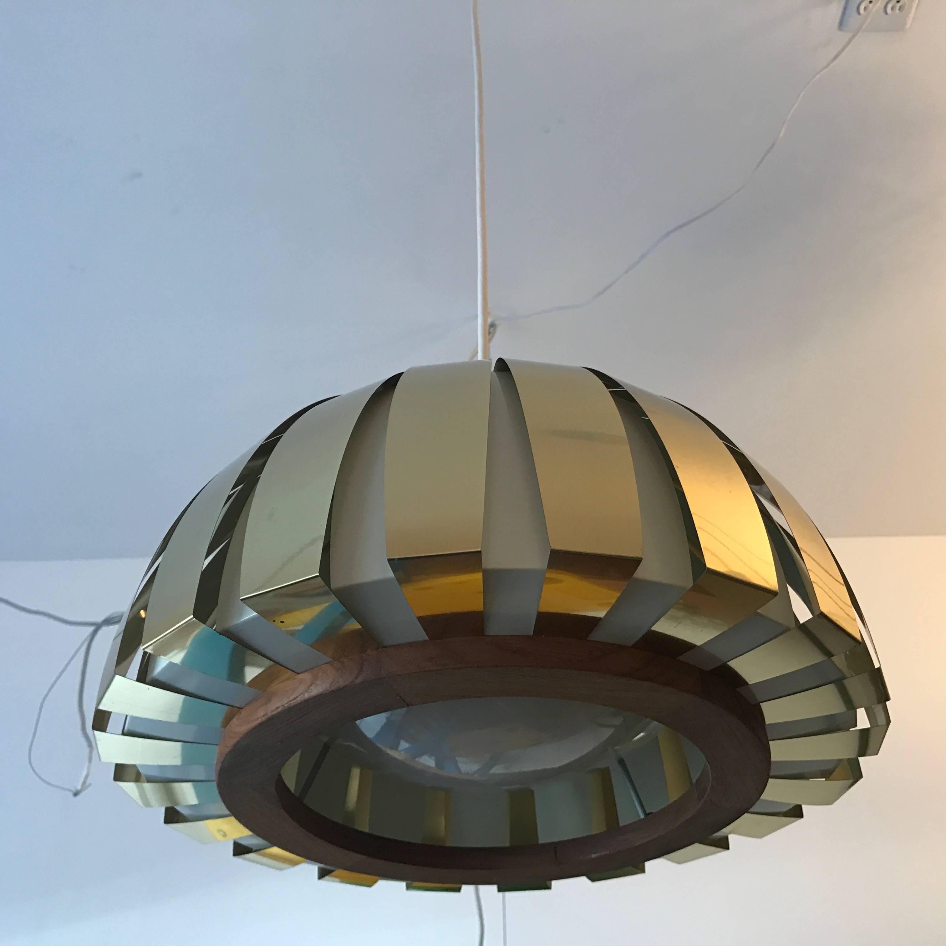 An original pair of new old stock Danish Modern pendants by Lyfa. The pendants are composed of polished brass and white enamel ribbon frames with teak accents and a white resin disk diffuser.