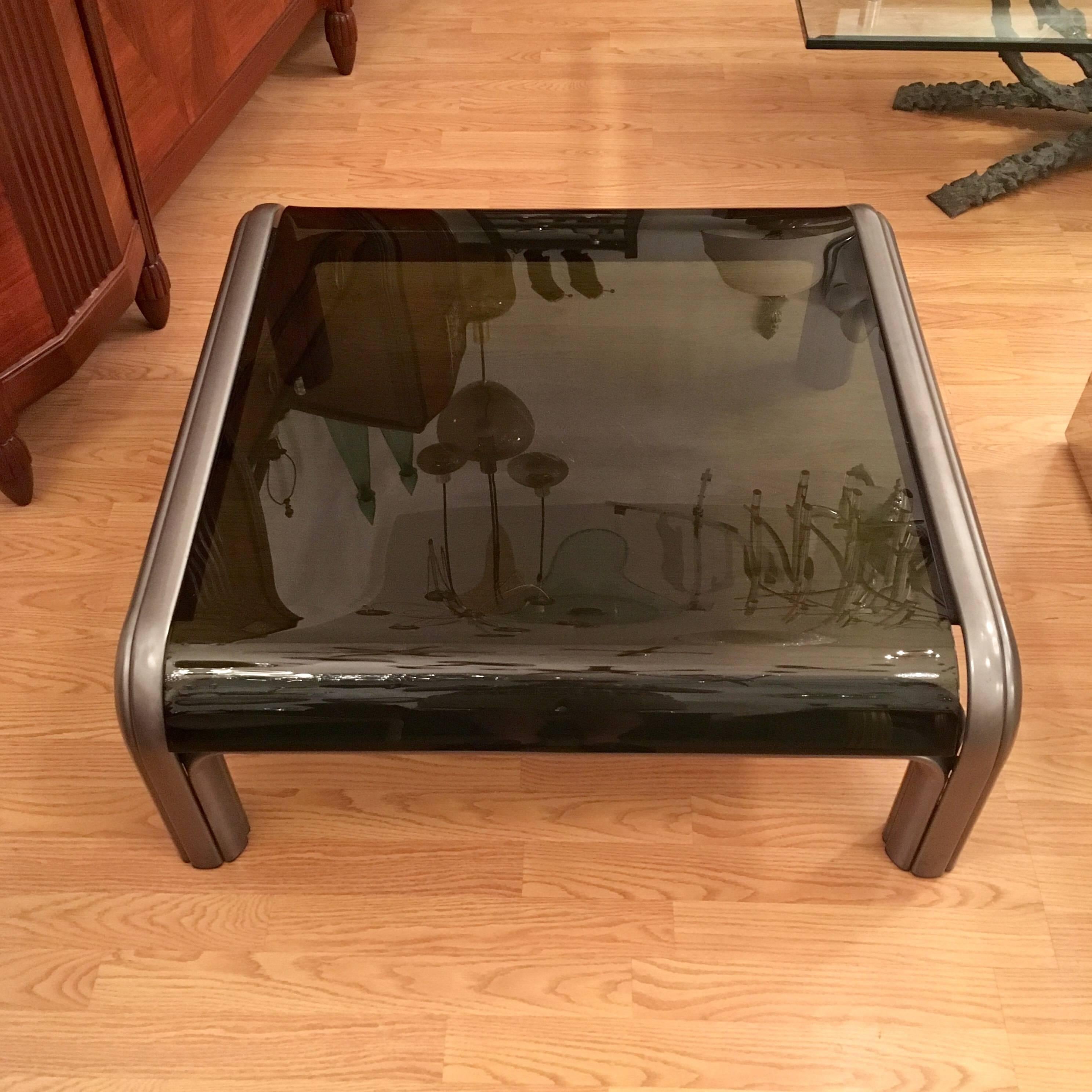 A Gae Aulenti designed for Knoll 1976 coffee table composed of a dark brown enameled steel frame and a curved dark smoked glass top.