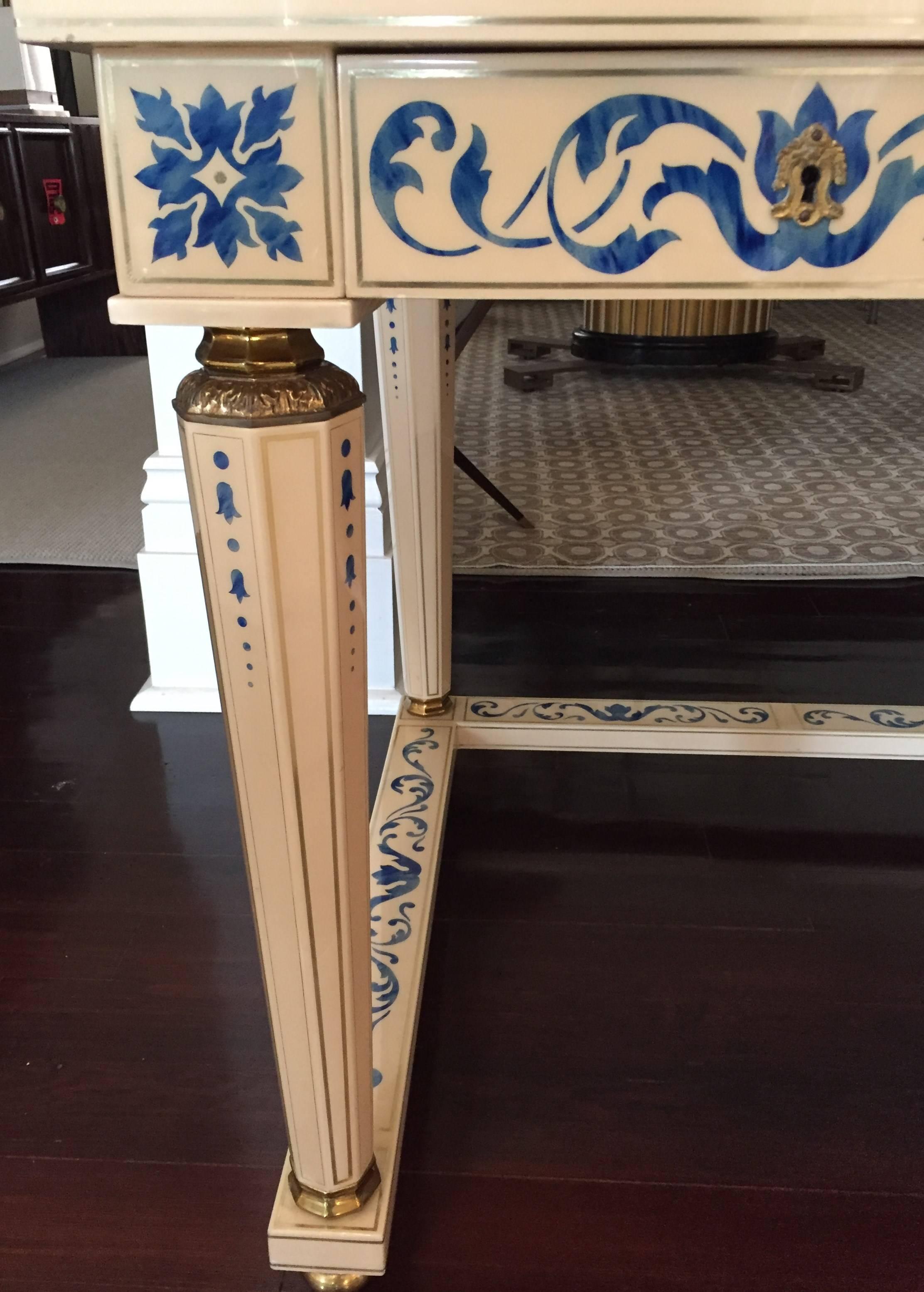 Three-drawer writing table in celluloid resembling ivory; stenciled in foliate patterns to suggest lapis lazuli; tapering octagonal legs joined by a C-shaped stretcher, also stenciled; details at the feet, columns, and escutcheons in polished brass;
