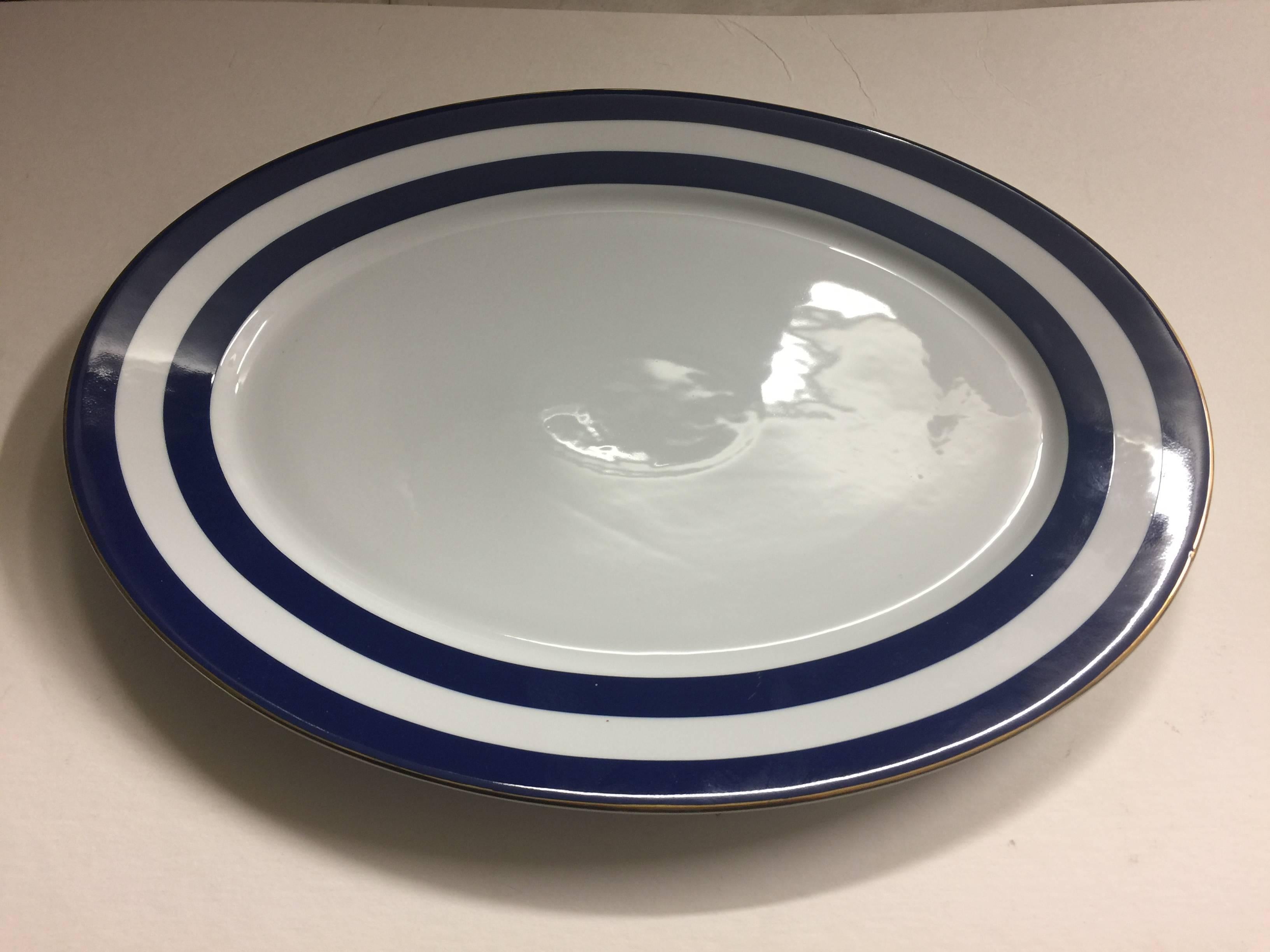 A porcelain serving platter in the Spectator Cadet pattern by Ralph Lauren Home Collection for Wedgwood. Signed, circa 1995-1996.

Features a dark blue double stripe on white with gold rim. Measures: 16.25 inches L x 12.75 inches W.
 