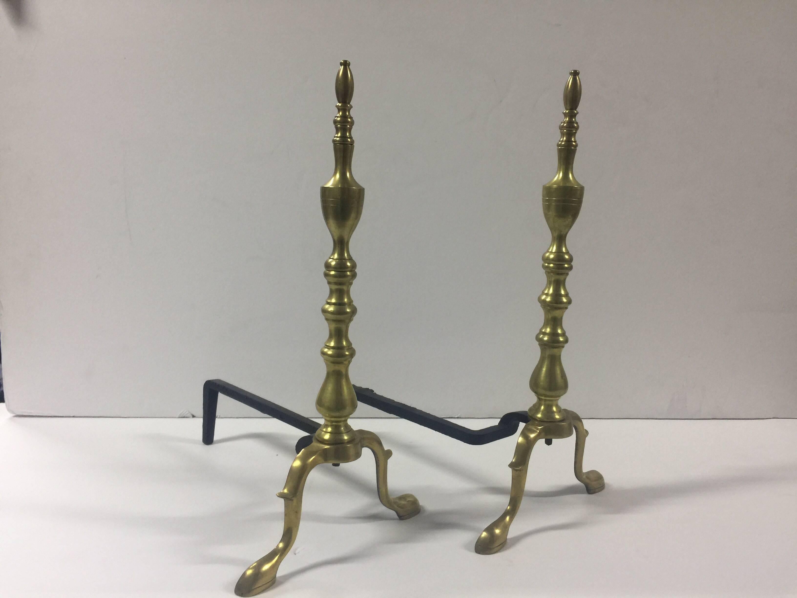 Set of polished brass andirons in a traditional style, USA, circa 1940. Black iron log supports.