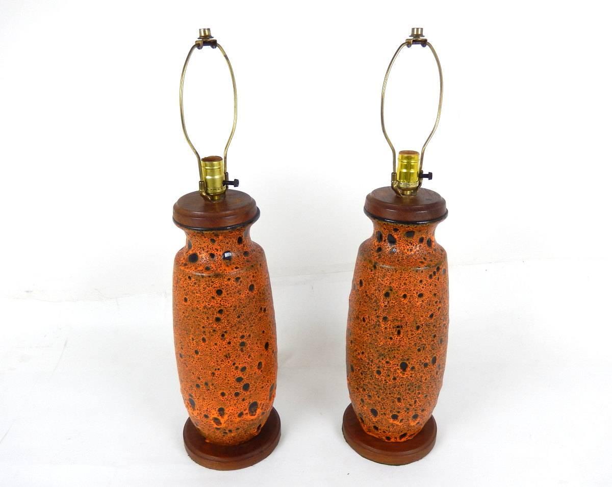 Crafted during the early 1960s, this pair of Mid-Century Modern table lamps feature large pottery bases finished in a thick bubbling orange and black lava glaze with teakwood caps and bases.

  