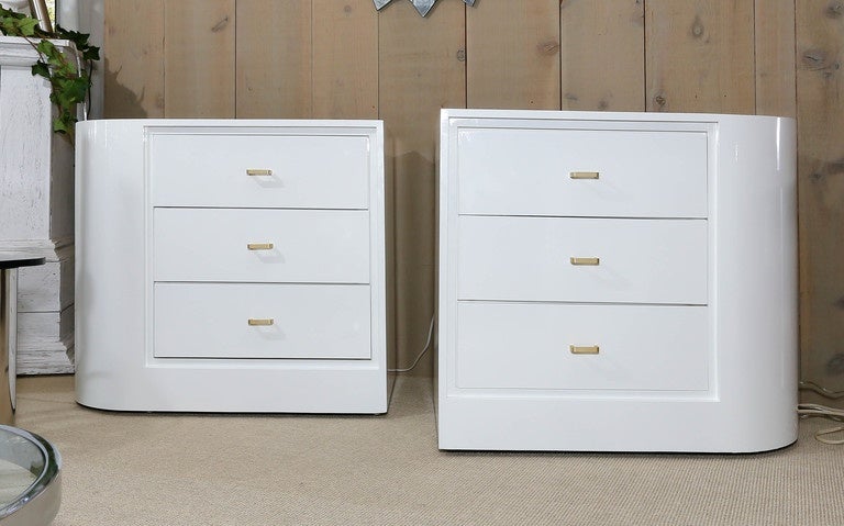Unusual pair of white lacquer Mid-Century three-drawer nightstands. The sides are rounded creating a right and left nightstand. They have brass drawer pulls.