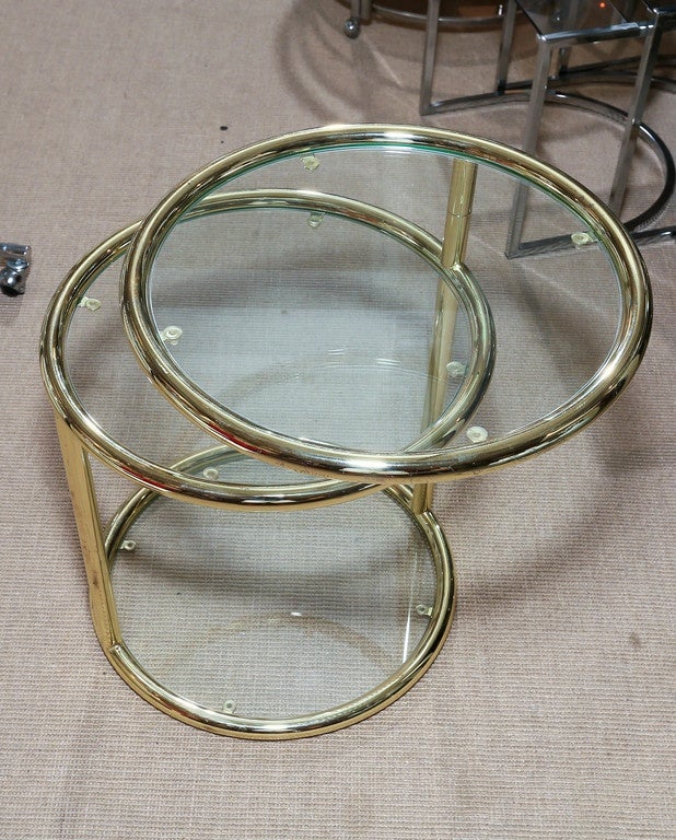 Attractive pair of Mid-Century brass three-tier mechanical tables. The tables have three glass shelves and the top shelf rotates.