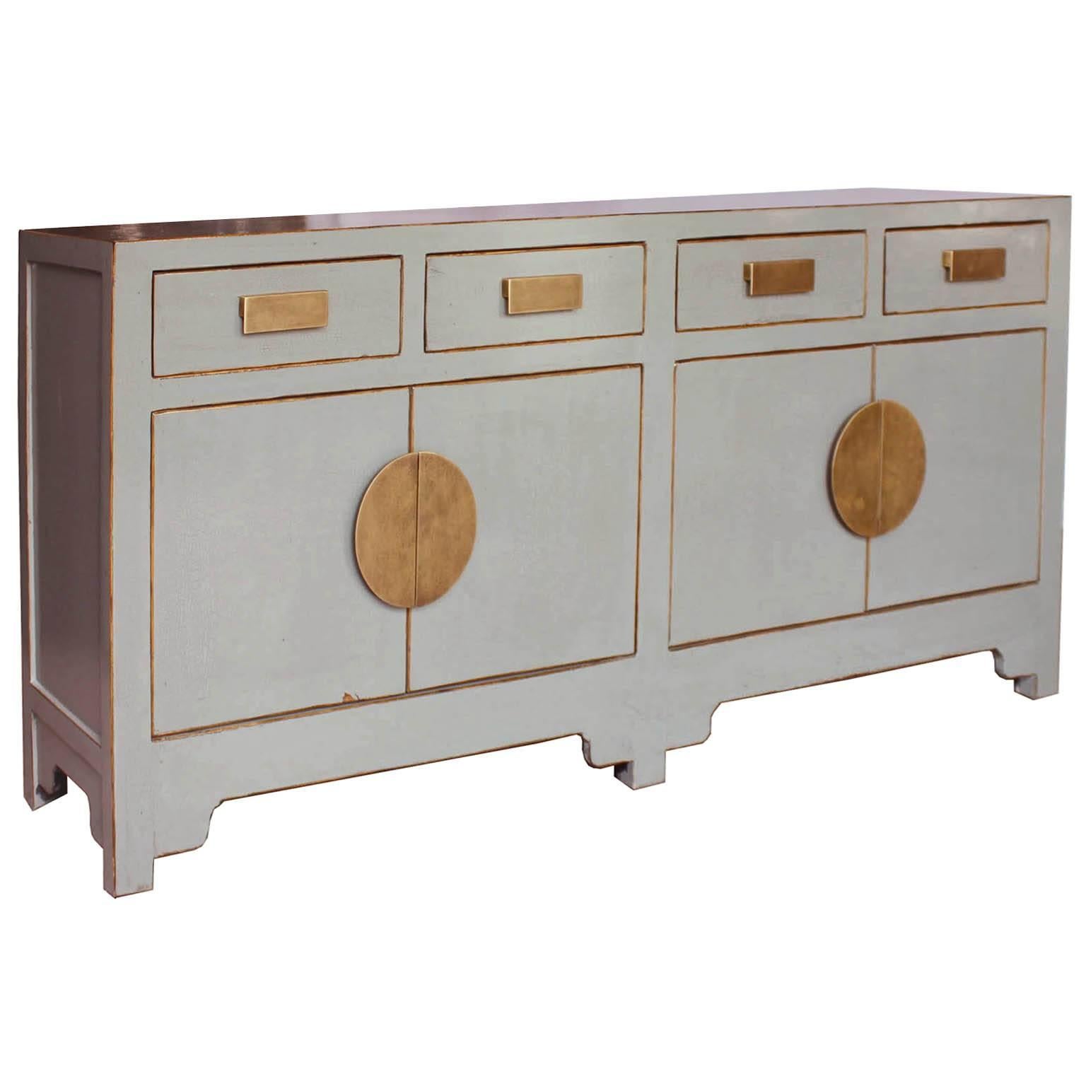 Place this gray sideboard with subtle crackle finish, bold brass hardware, exposed wood edges and clean lines in a modern living or dining room as a focal point.