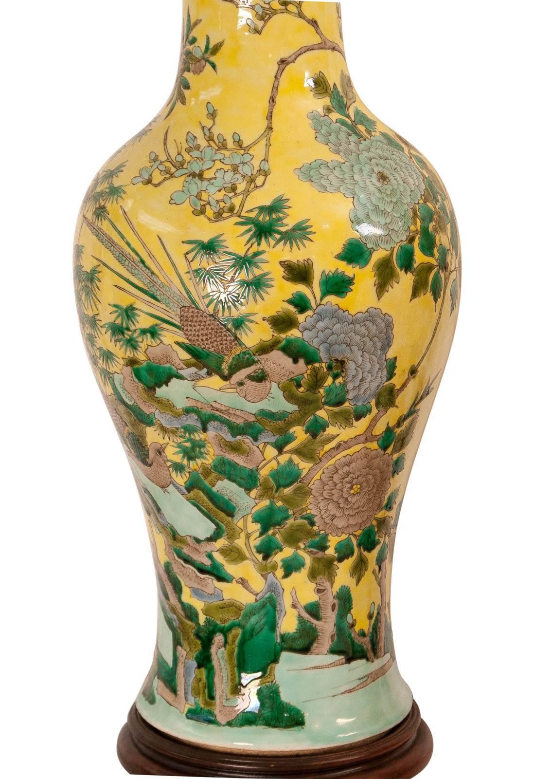 A large pair of yellow ground Chinese porcelain vases made in the Kangxi style during the Republic period, circa 1915. Decorated all-over in greens, pale blue and grey with birds and flowers. Now mounted as large lamps on hardwood stands. One vase