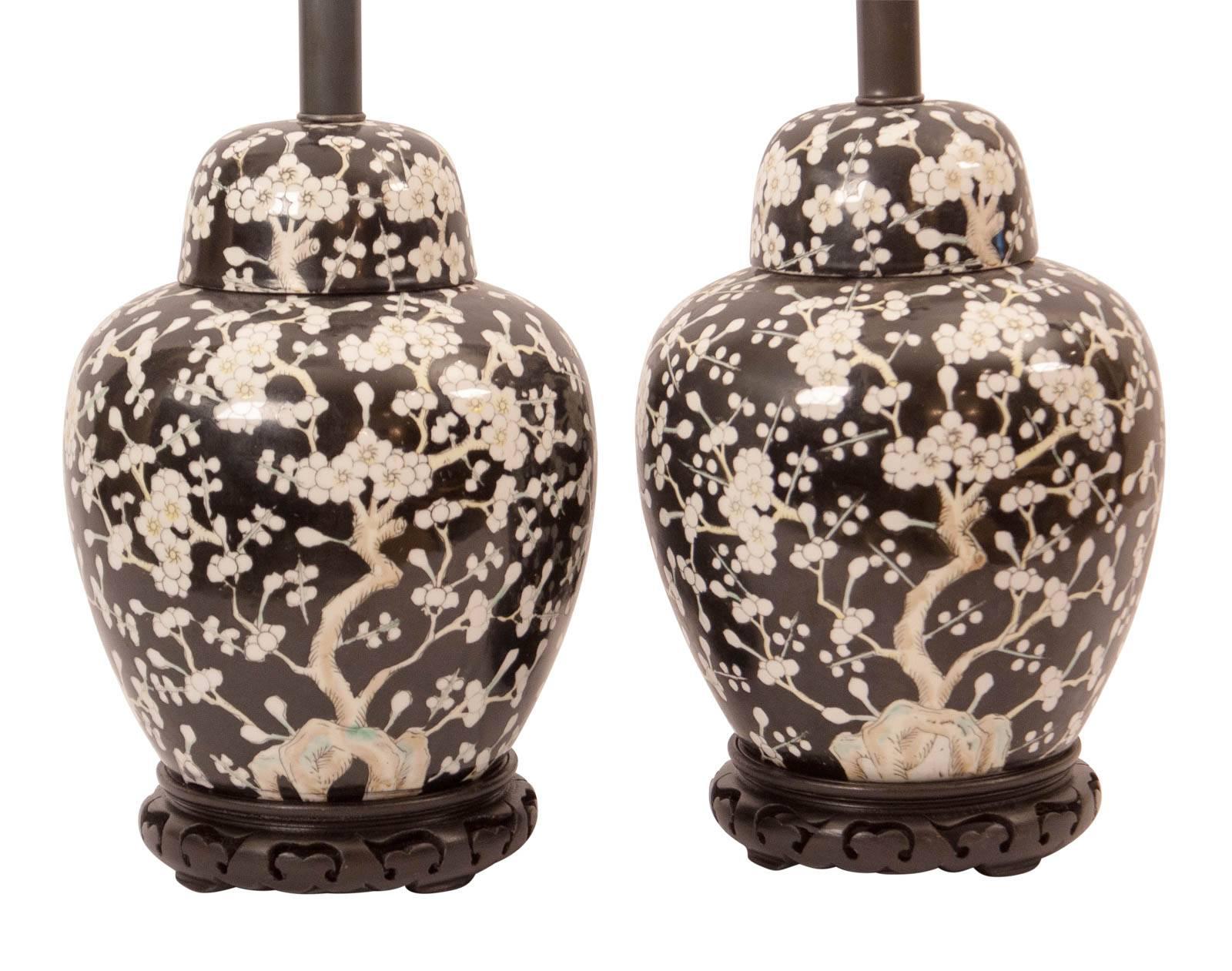 Pair of ginger jars with covers painted with flowering prunus on a black ground. Mounted as lamps on a carved wood base with new wiring, China, circa 1960.