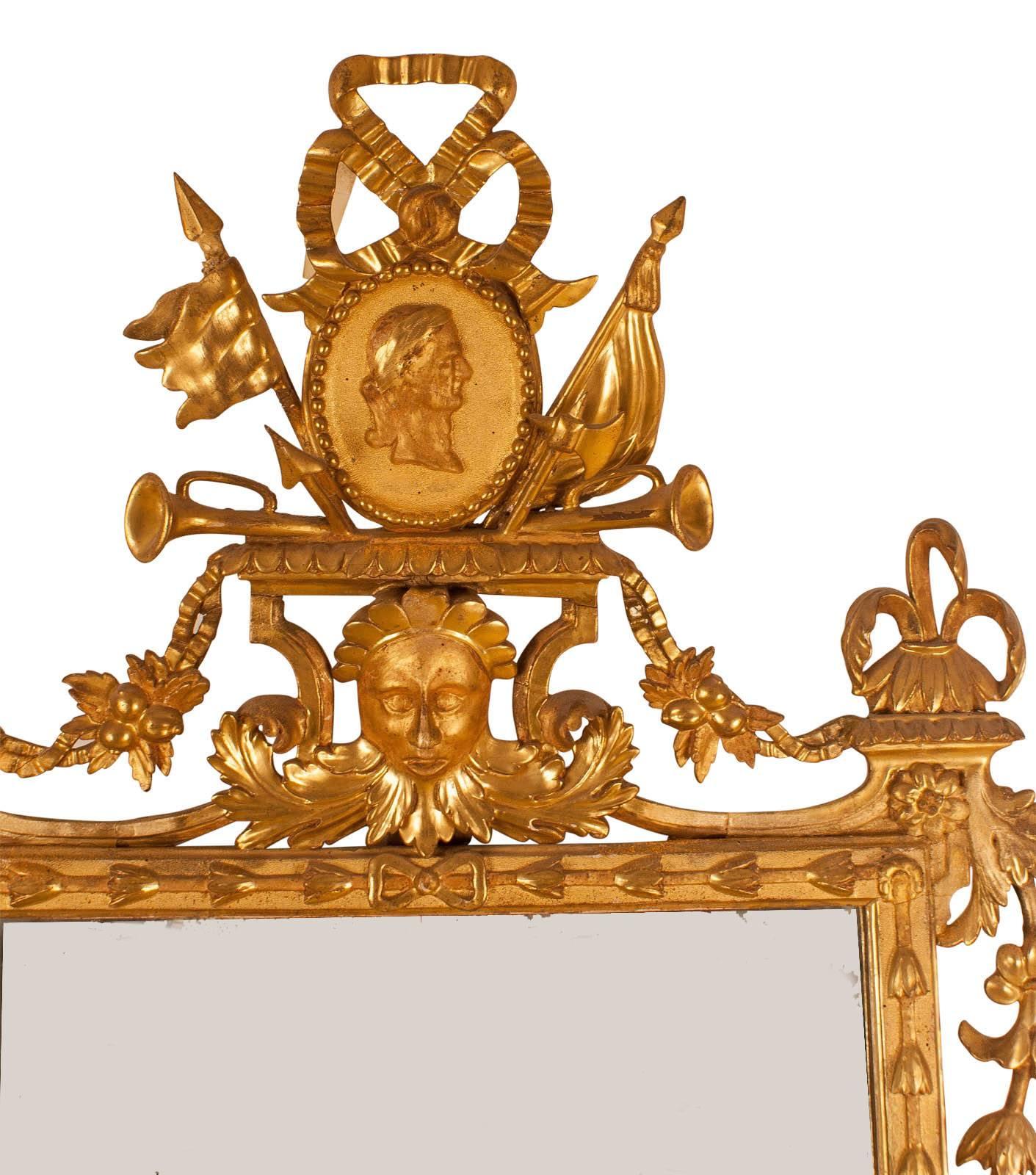 A large and well carved and gilt wood mirror made in Italy, circa 1810. With trophies, swags, urns and masks. Some small repairs to gilding, plate later. A wonderful large and decorative mirror.