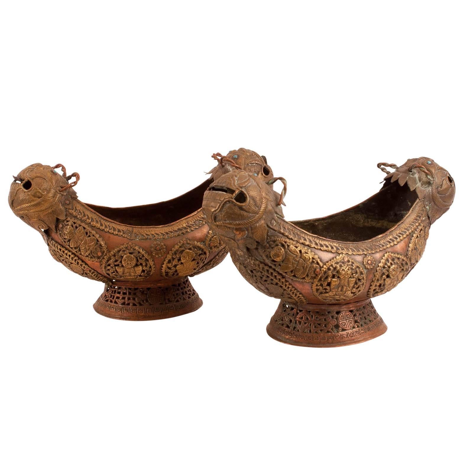 A very unusual pair of boat shaped footed bowls in hand worked copper with brass appliques of deities and auspicious symbols. Each end with a 