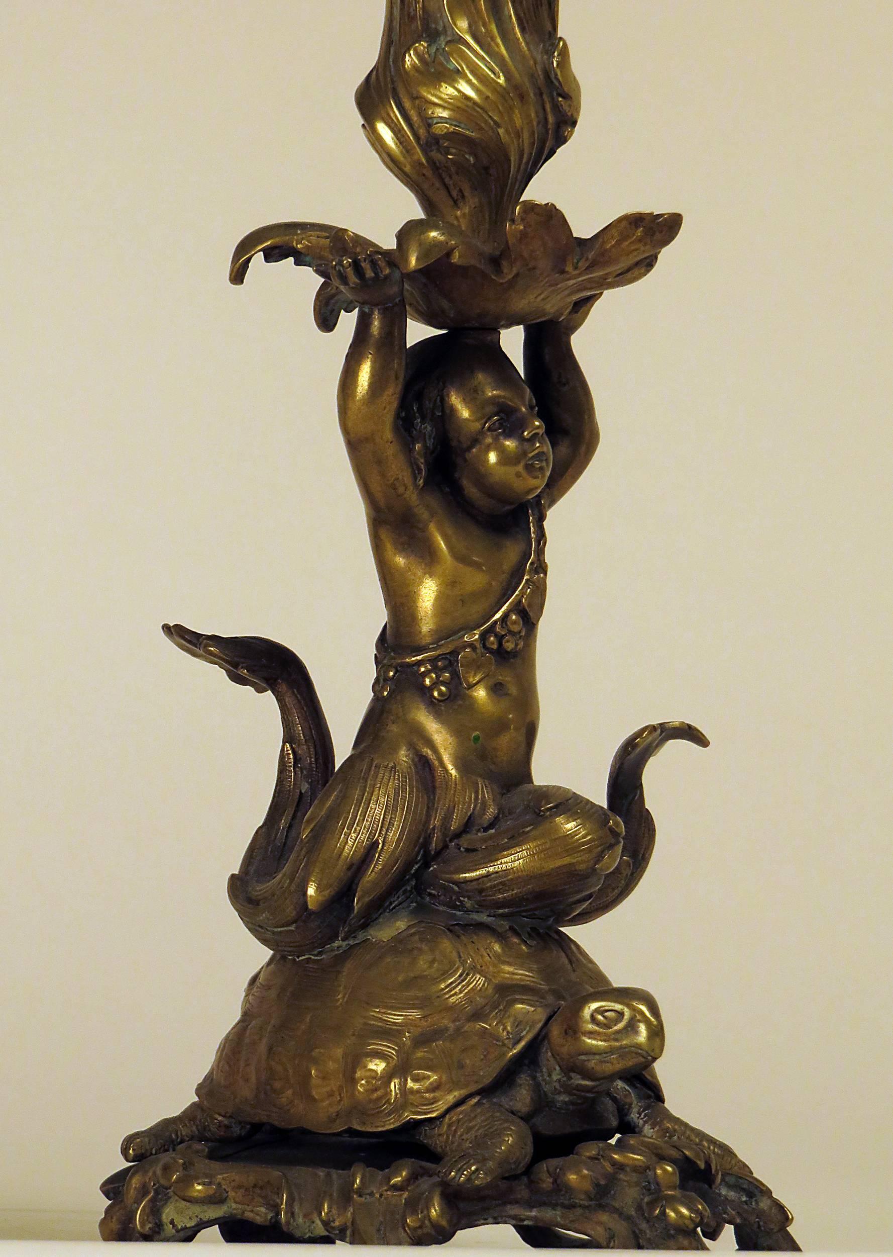 A wonderful large pair of bronze candle sticks cast as young sea nymphs riding a turtle on a scrolling weighted base. Raised arms support candle cup and bobeche. From a very good West coast collection assembled about 1900. The casting and sculpting