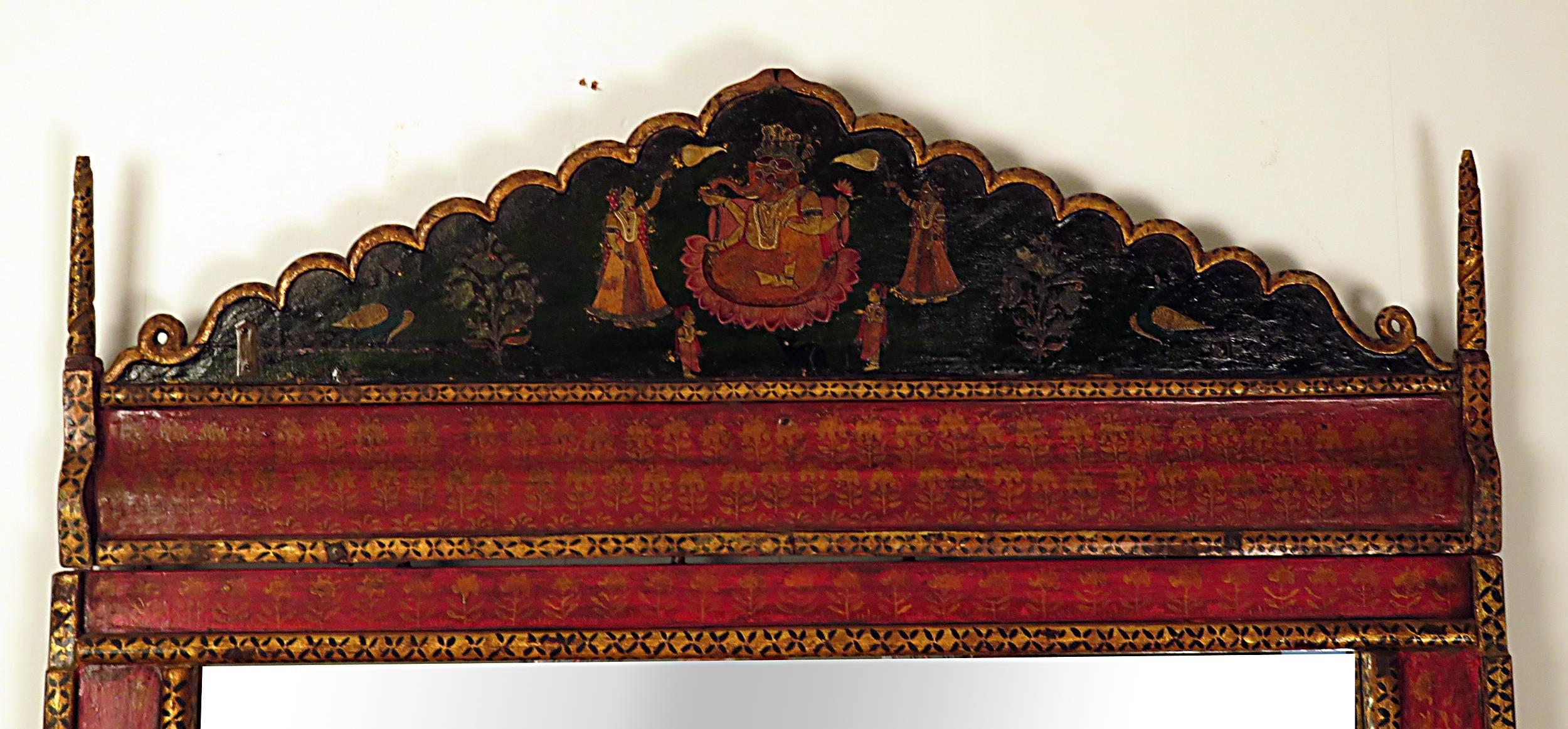 19th century Indian architectural element featuring Ganesha with two attendants later mounted on the crown of a custom matching mirror frame. Painted in brilliant reds and deep green with gilt accents.  Very dramatic and sophisticated mirror.  Nice