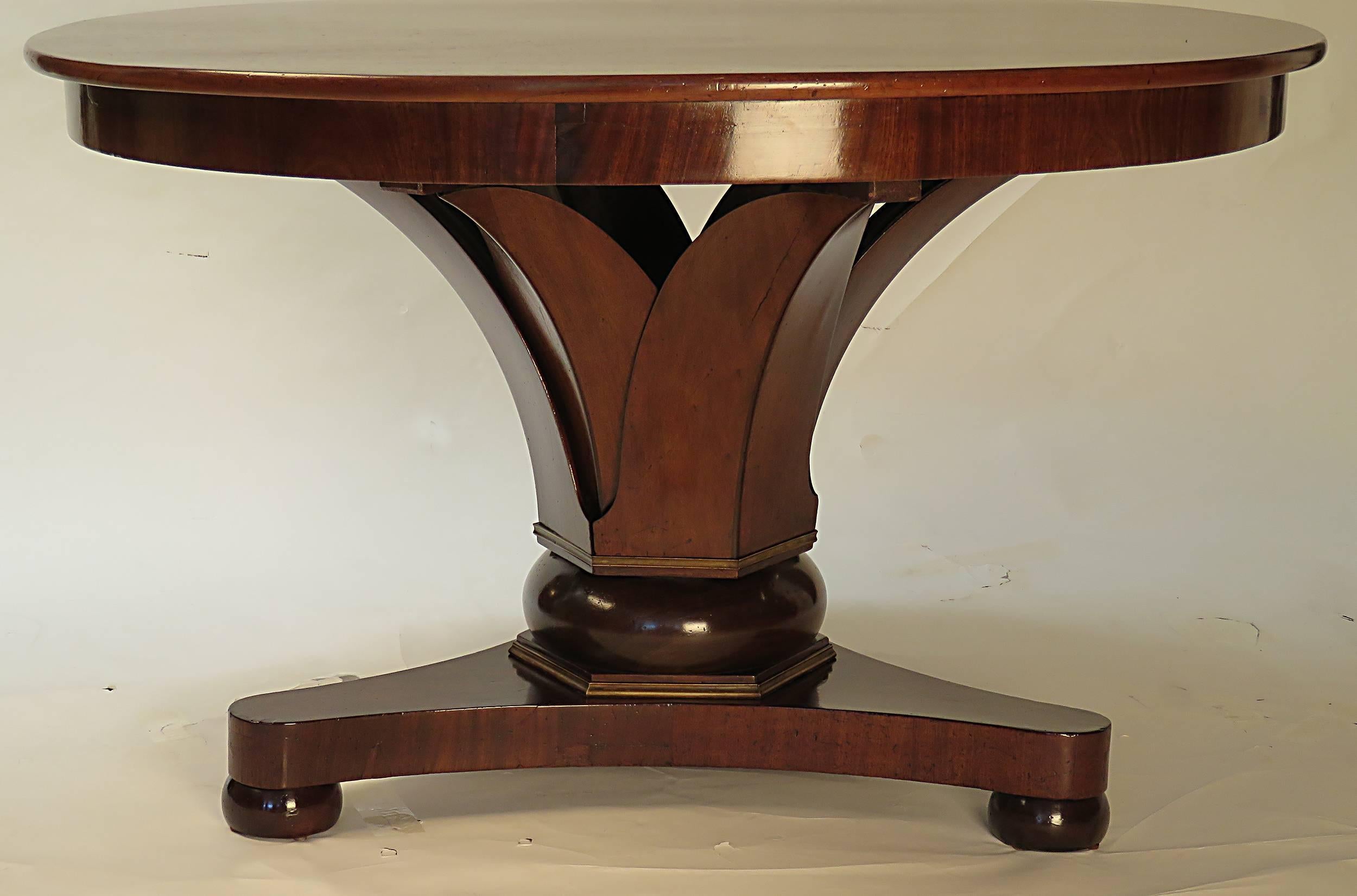 A very elegant 19th century round center table supported by stylized leaves rising from a compressed bun, framed top and bottom with gilt metal accents, standing on a tripod base with compressed bun feet. A mix of fruitwood, mahogany and boxwood