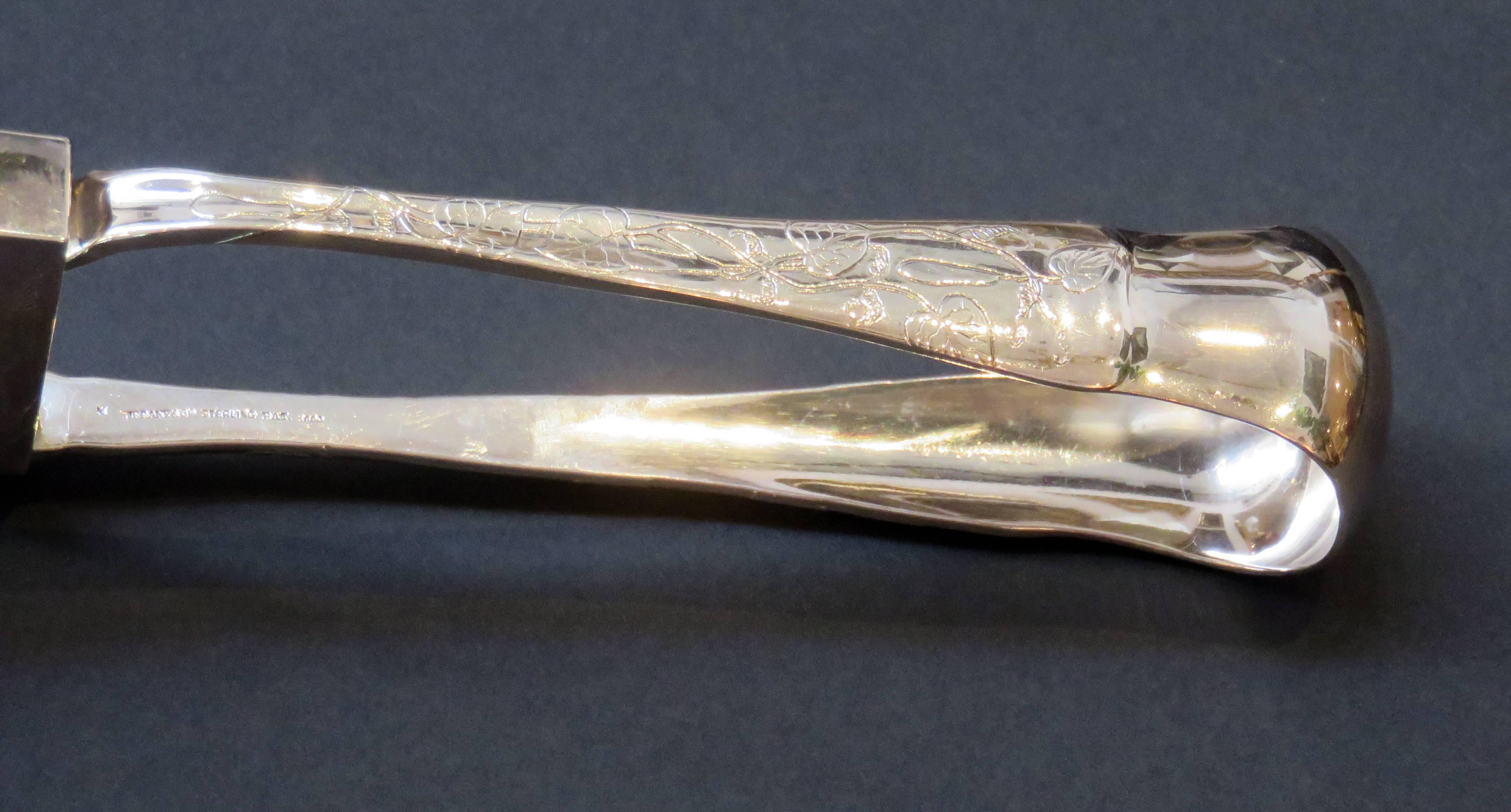 A Tiffany & Company sterling silver lap over edge acid etched asparagus tongs in the yoked bow style. Engraved with a stags head on the end. Marked Tiffany & Company Sterling Pat. 1880, the date letter 
