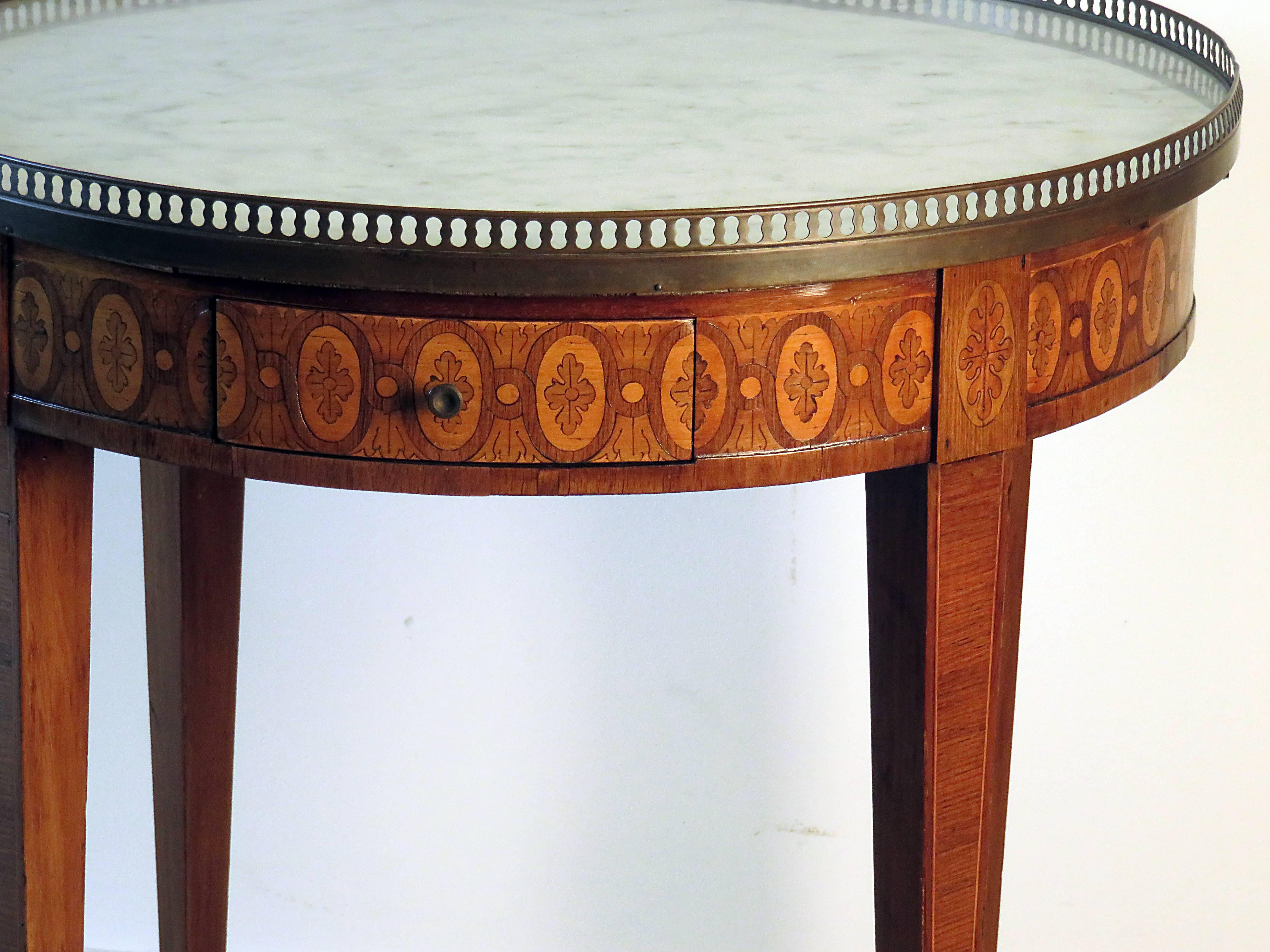 A Classic French round side table on square tapered legs with brass caps. The top has two opposing drawers and two opposing candle slides with leather top. The marble top has a pierced brass gallery with a couple of small losses. The inlay is