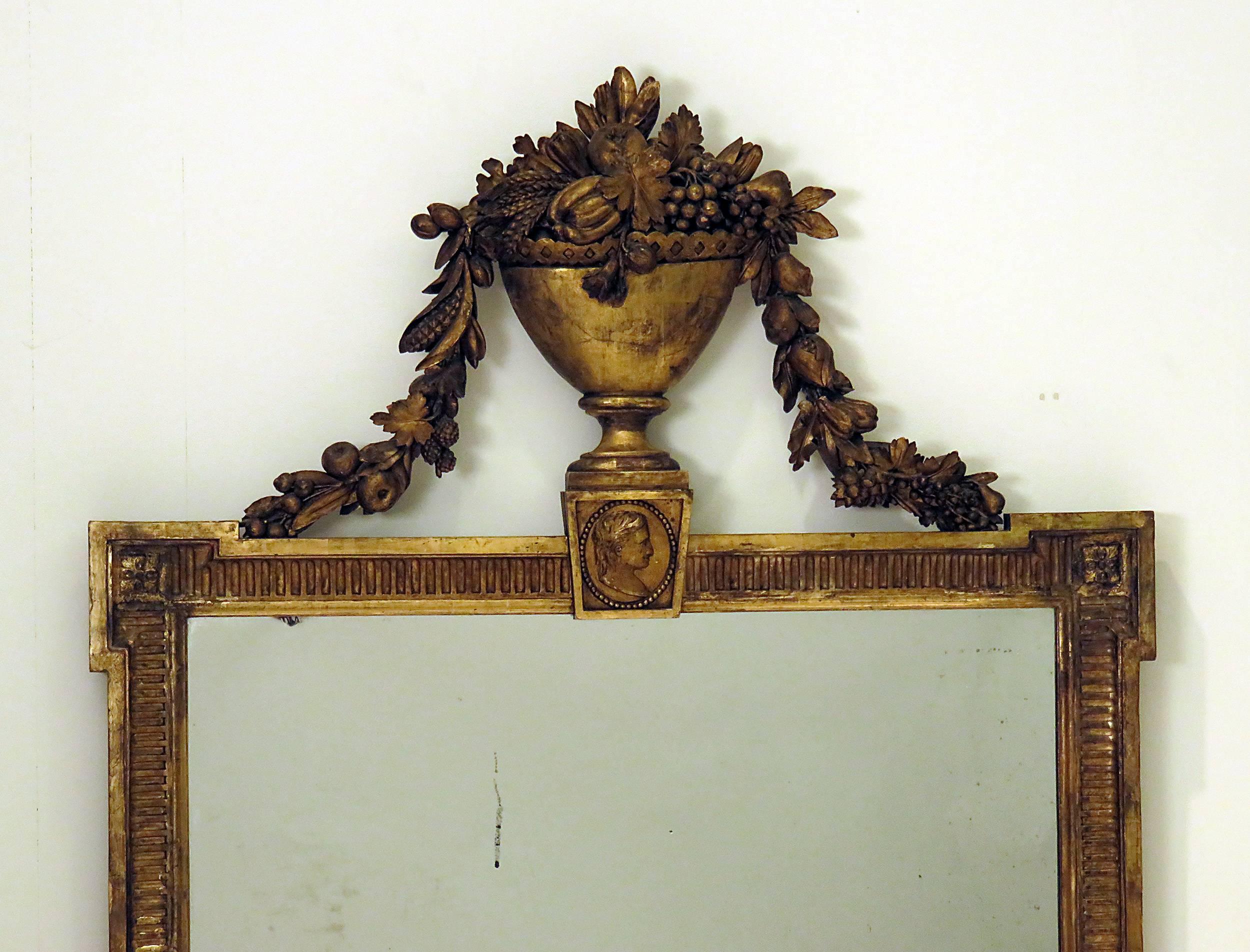 A 19th century French or Swedish giltwood over mantel mirror, circa 1820. The mirror has an urn with garlands flowing down to the top of the mirror. Below the urn is a bust of a man. The frame is deeply carved and the gilded surface has nice color