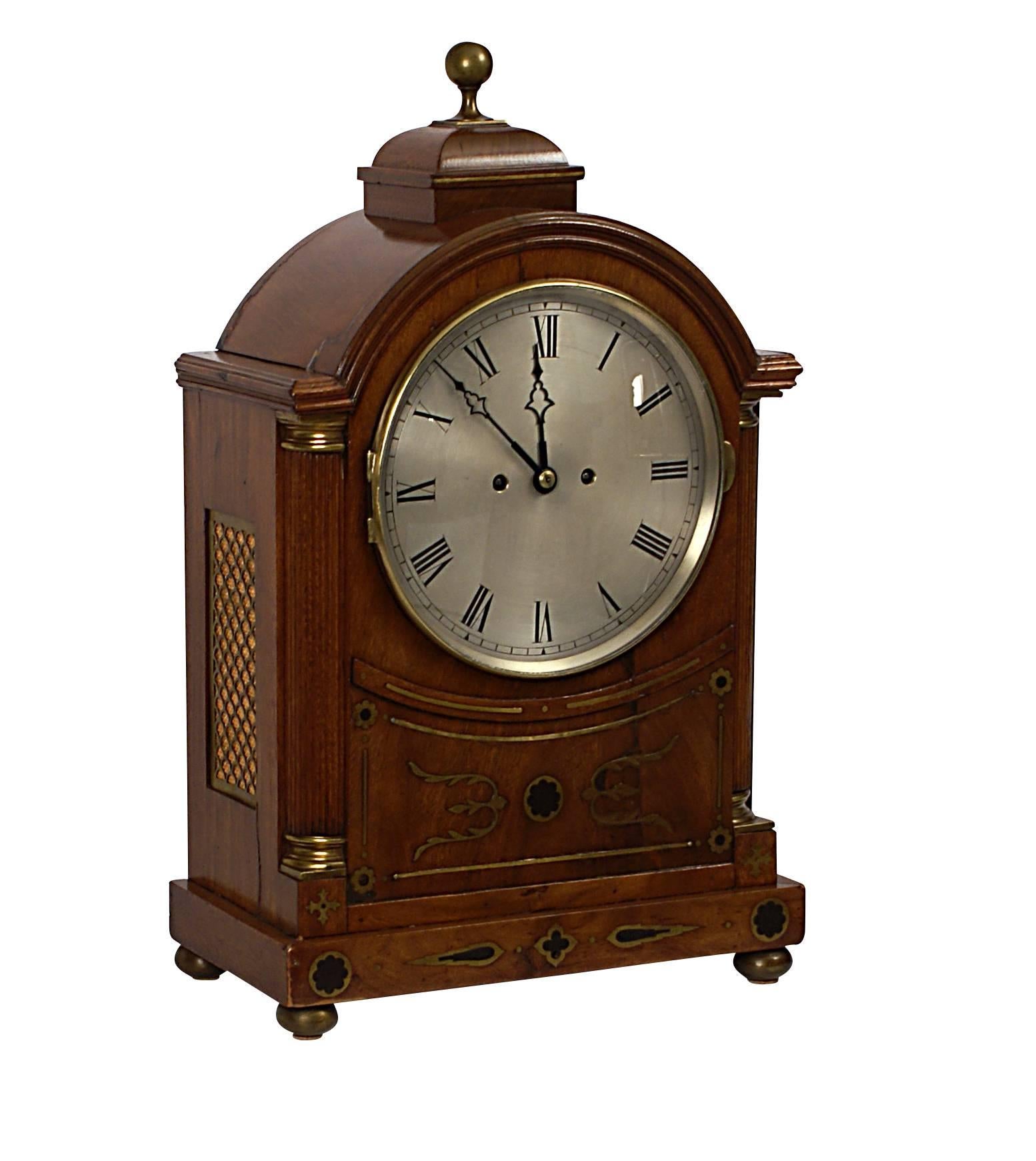 A handsome English Regency period mahogany bracket clock. Inlaid with brass and ebony. The arched dial framed by brass capped fluted columns. The inlays reference neoclassical and Gothic themes popular during this period. Made, circa 1820.