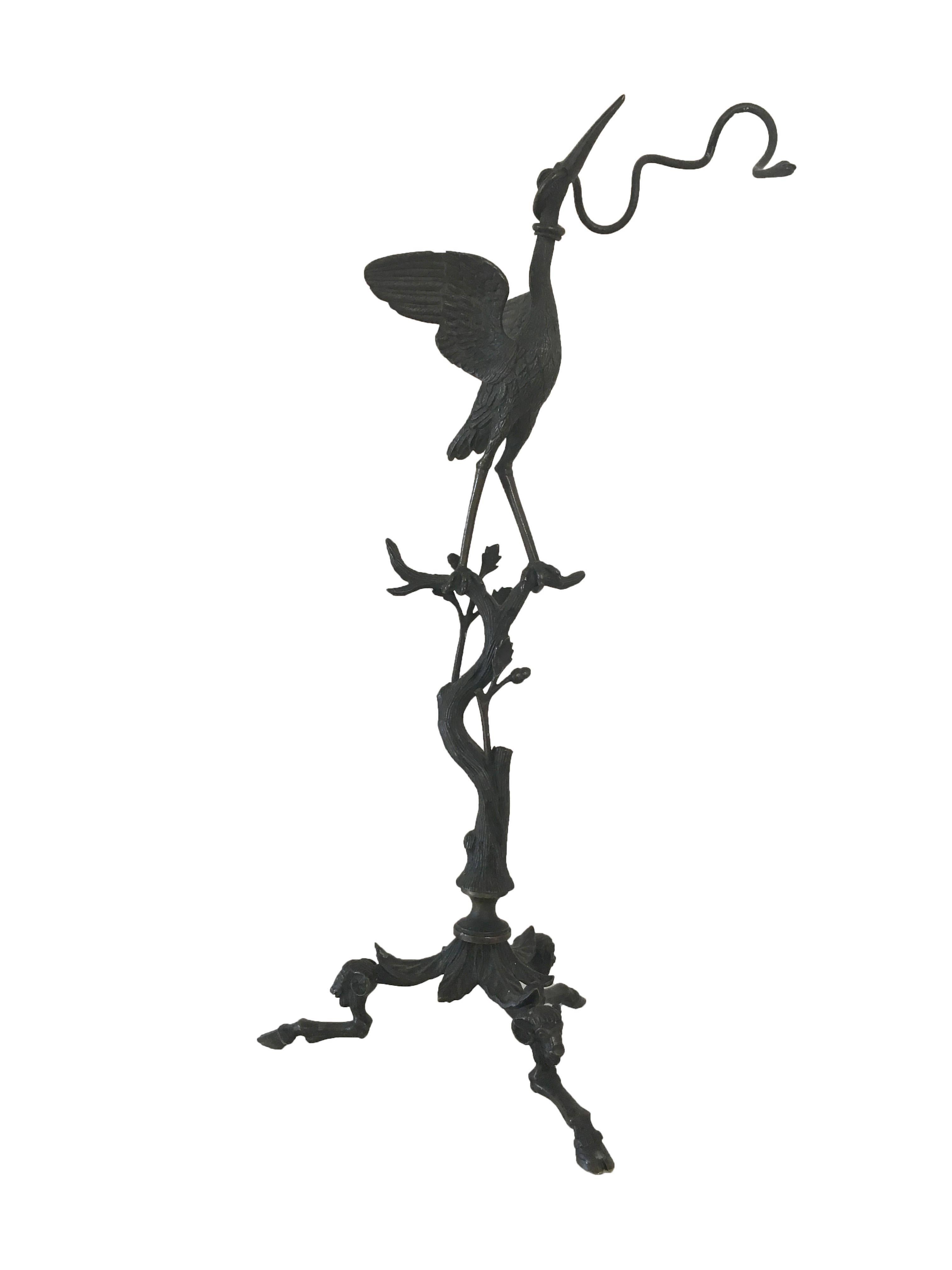 Bronze stylized sculpture of a stork holding a branch in the beak, with additional branch detailing below and on hooved feet.