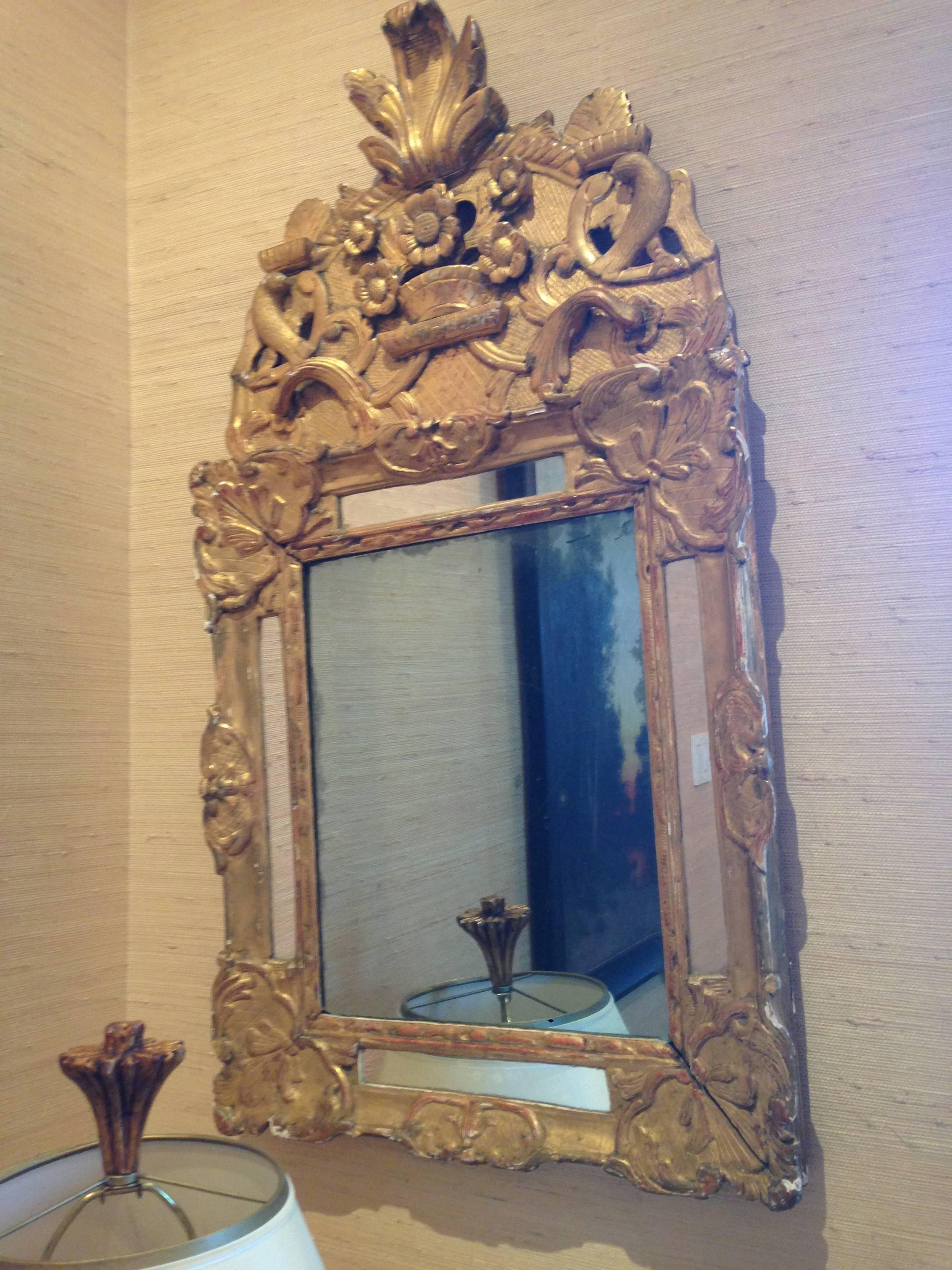 Beautiful early 18th century French Regence giltwood mirror featuring inset mirrored panels and topped by flower basket and acanthus leaf carvings, circa 1710.