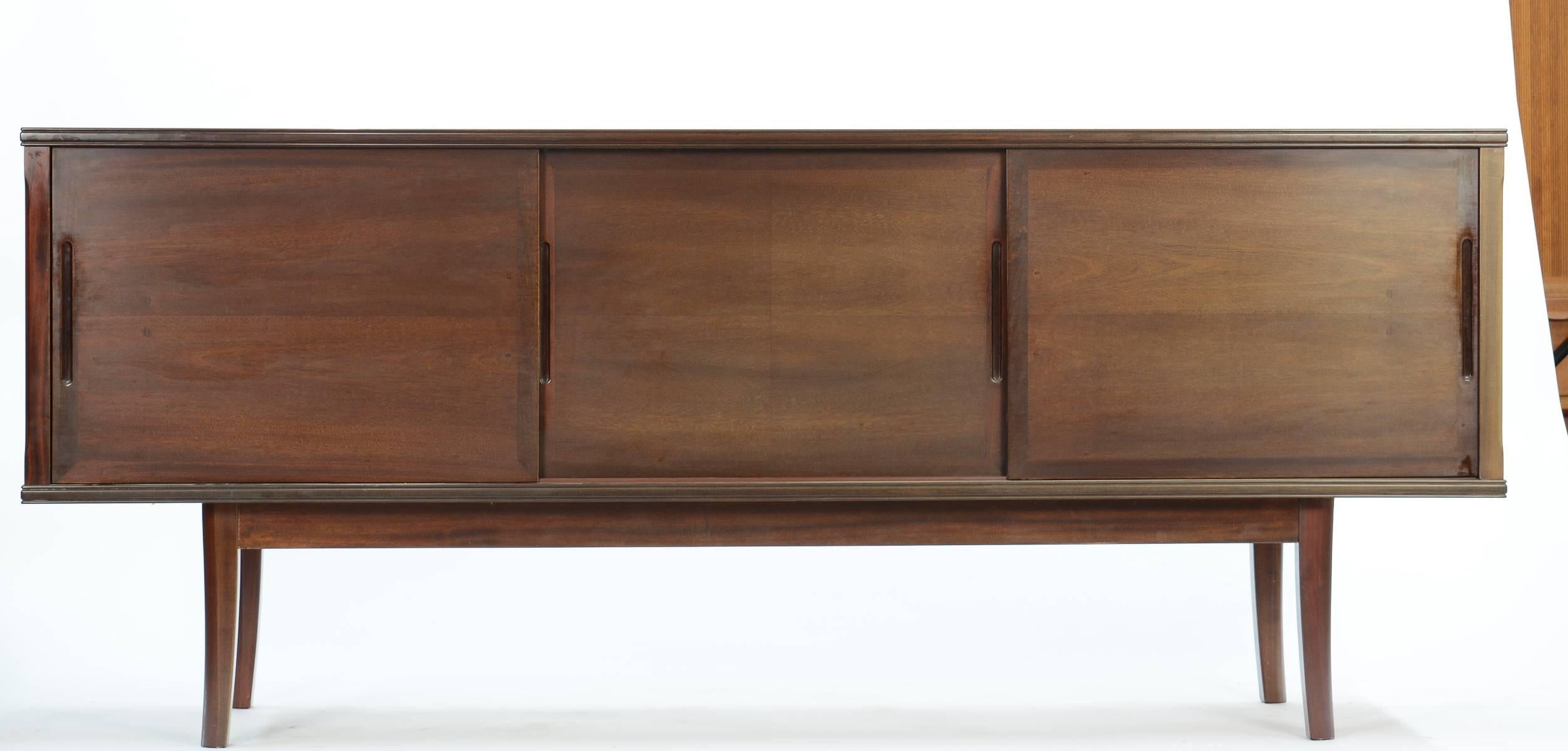 A grand sideboard in stunning solid mahogany by Danish master Ole Wanscher. Three sliding doors reveal two shelves on the left, two felted doors center and one shelf right. Grooved detail top and bottom adds unusual elegance.

Ole Wanscher