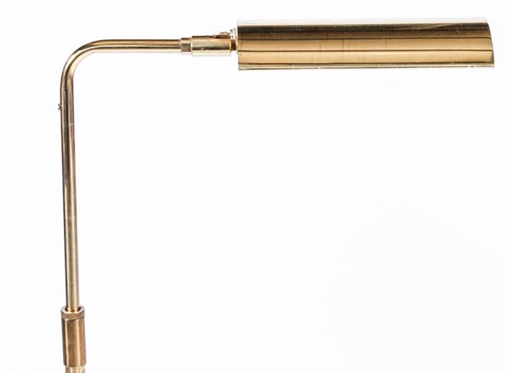 A Classic midcentury Koch and Lowy brass floor lamp, circa 1970s, with a half-round brass shade and a twist on/off knob switch. The neck of the lamp is bent at a 90-degree angle, holding a rotating, highly-Directional shade. The stem column is