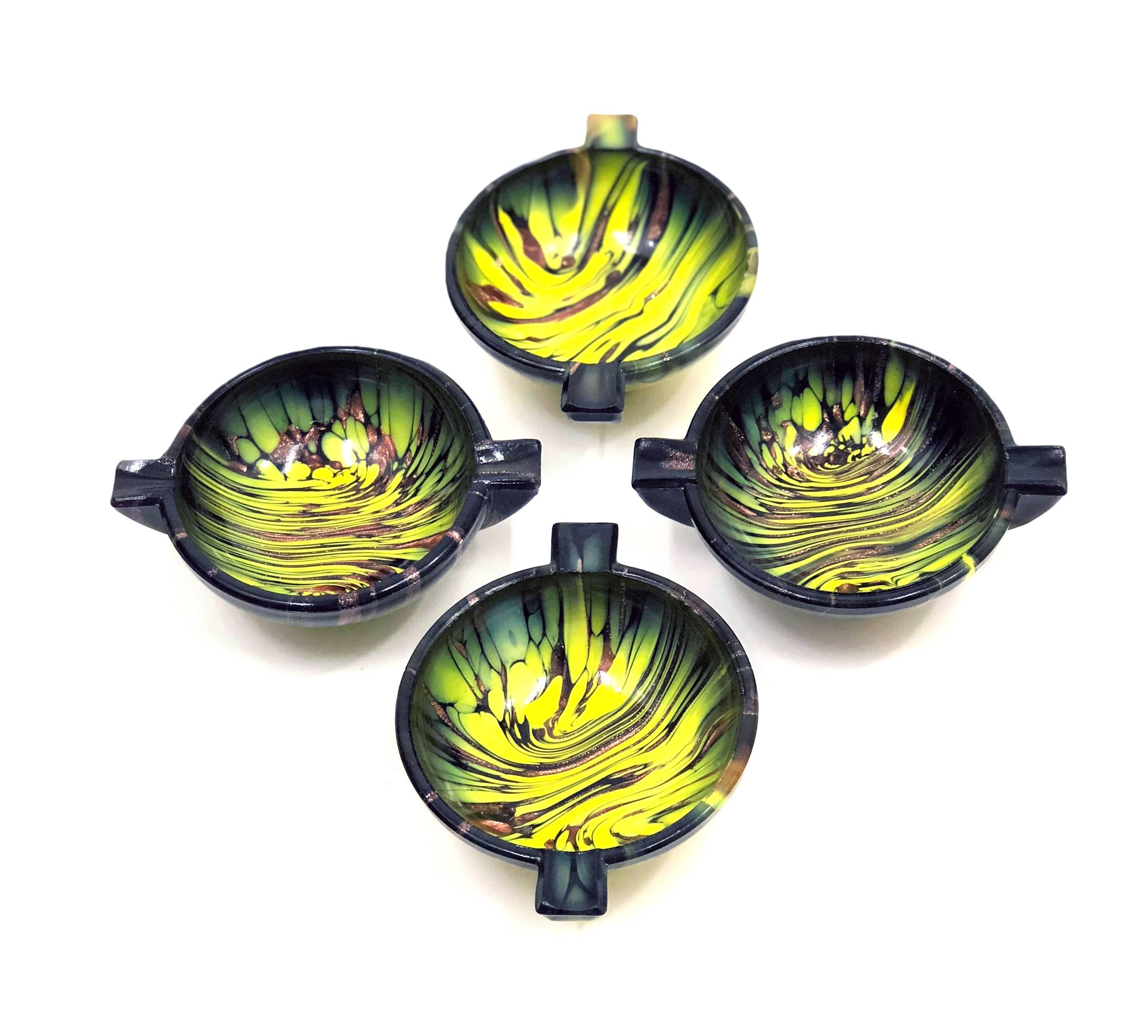 Four exquisite and truly beautiful Mid-Century Murano art glass ashtrays.  All are unused and in like-new condition, stored in their original box since the 1960s.  Dark glass with copper aventurine and swirls of yellow and moss greens, having the