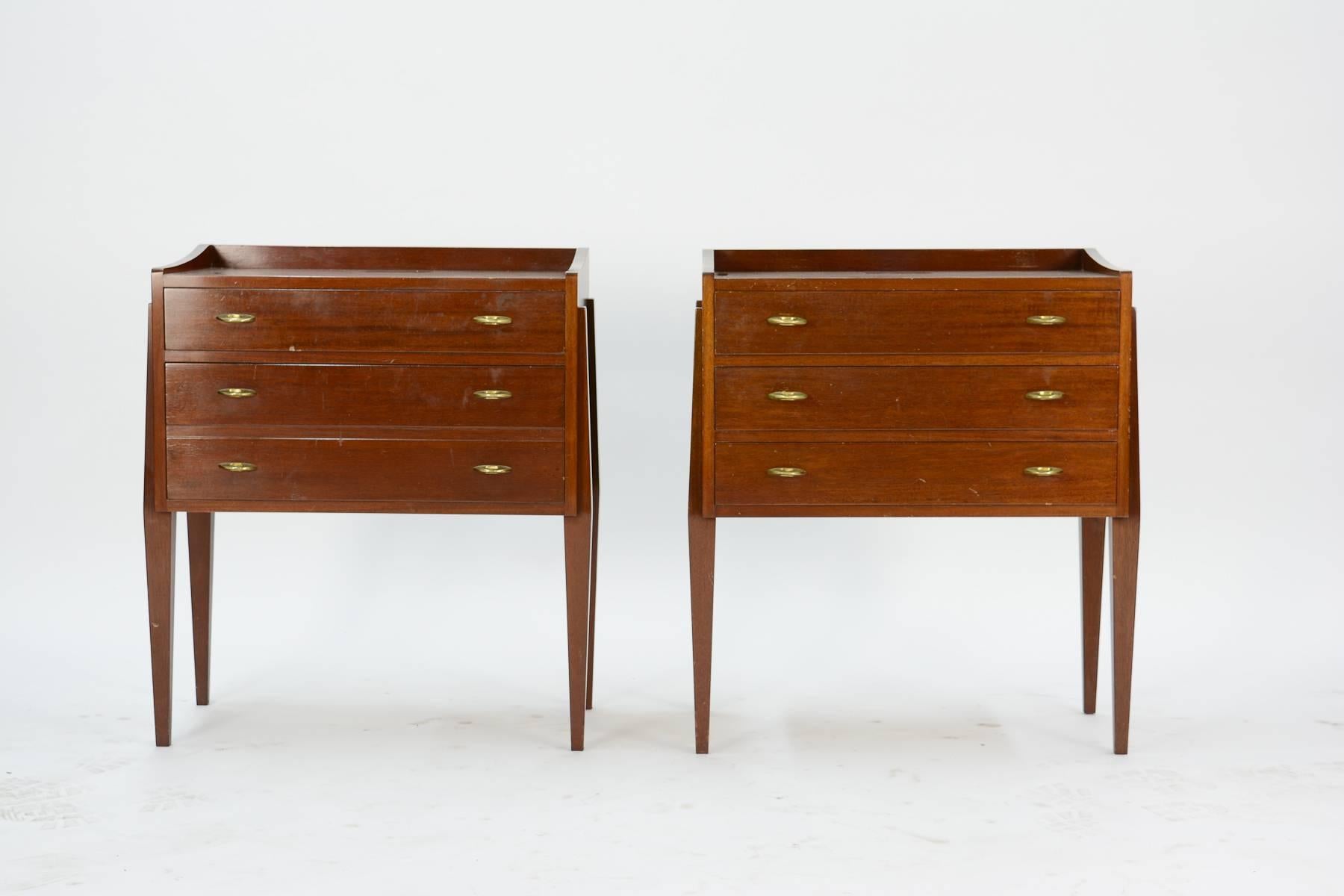 A wonderful pair of Mahogany chest of drawers, nightstands or end tables by Frode Holm for high end Danish furniture company Illums Bolighus of Denmark. The pair features brass pulls and tappered legs with three drawers each.