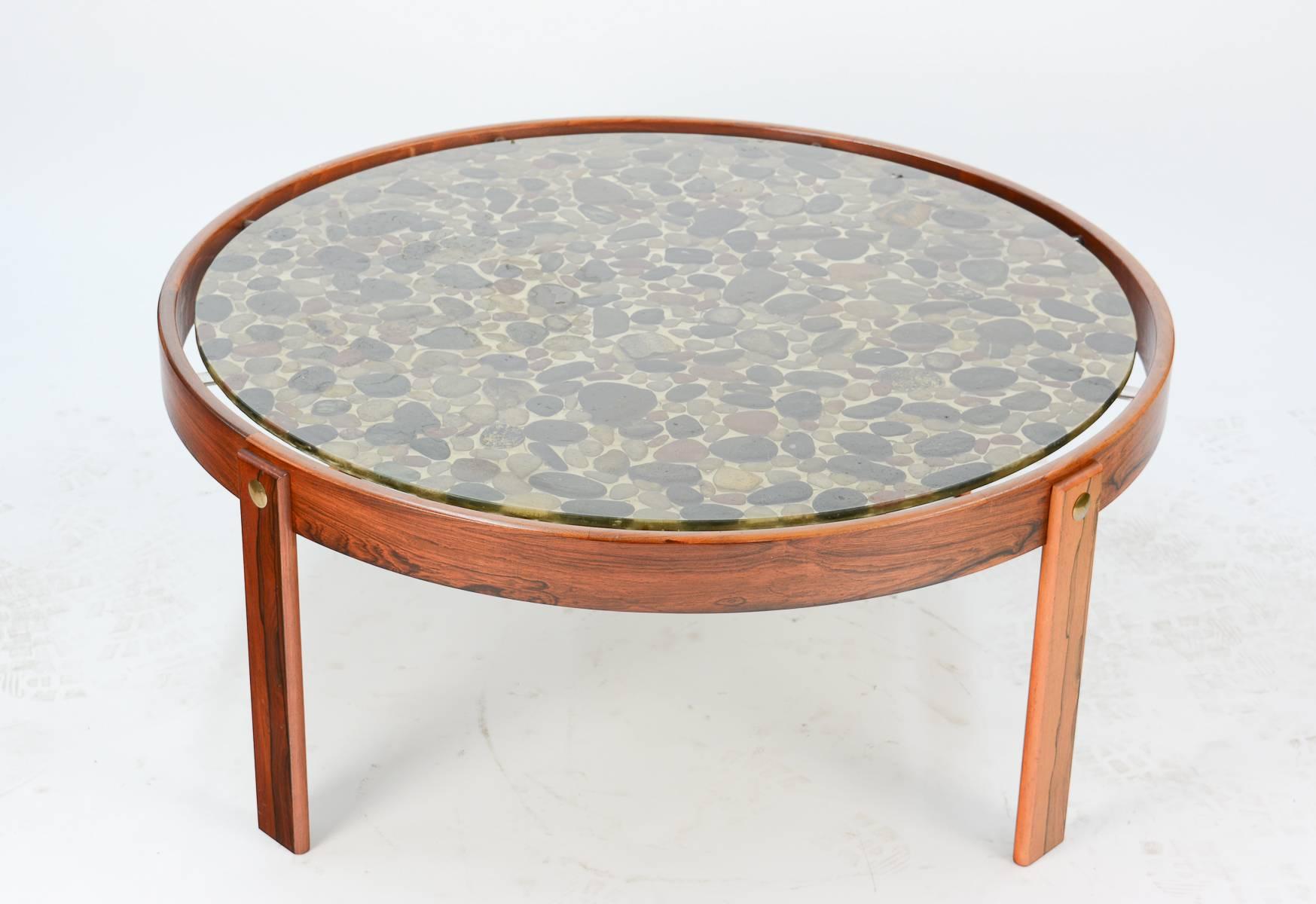 A beautifully uncommon and attention-getting Danish modern coffee table with river stones set in resin and elevated in a rosewood frame.

The floating, waterproof resin cocktail surface invokes the sensation of viewing stones at the bottom of a