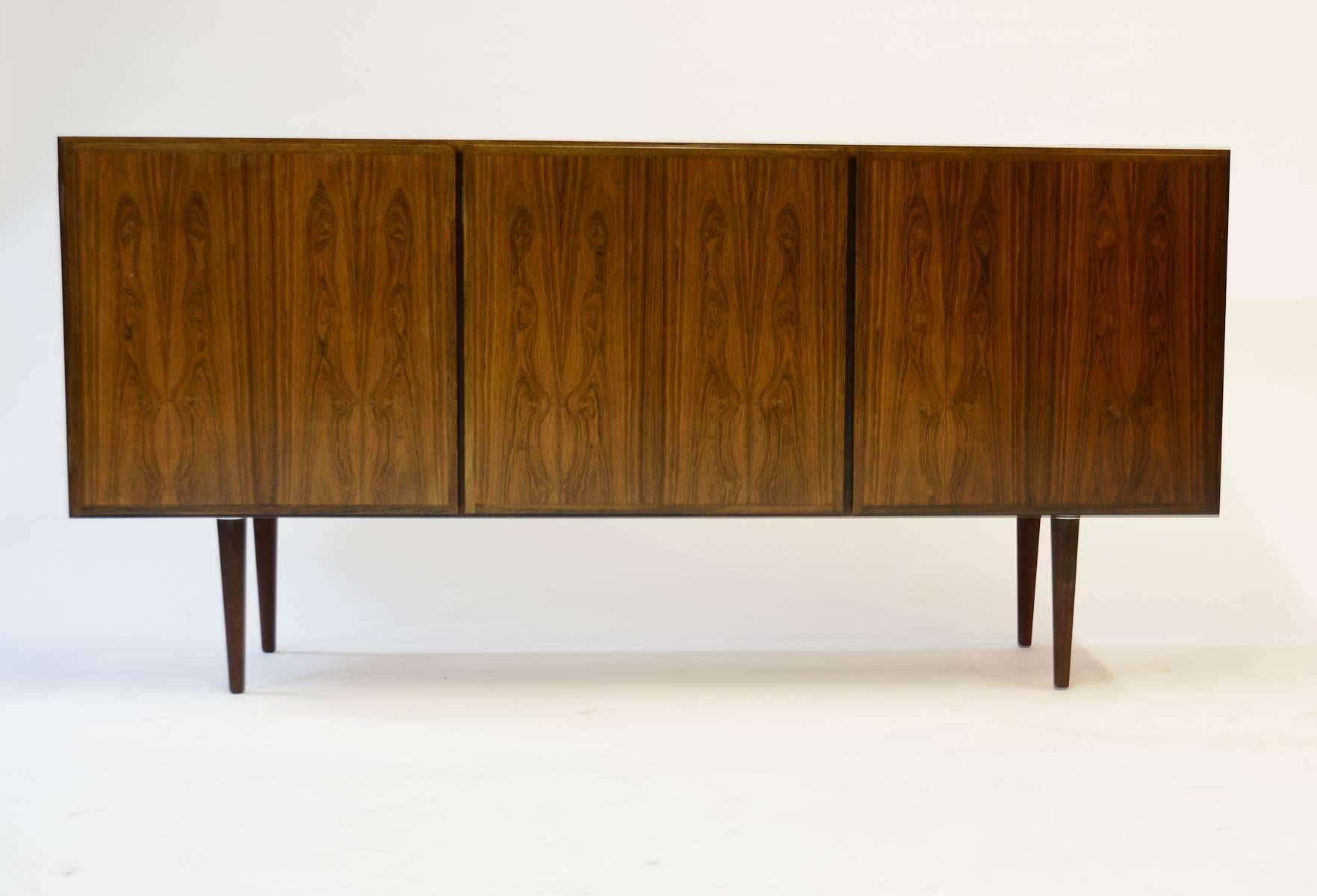 A finely-grained rosewood Model 30 credenza by Danish Mid-Century designer Gunni Omann for Omann Jun.

Upper drawer and adjustable shelf in the left compartment. Double adjustable shelves in the centre and right compartments.