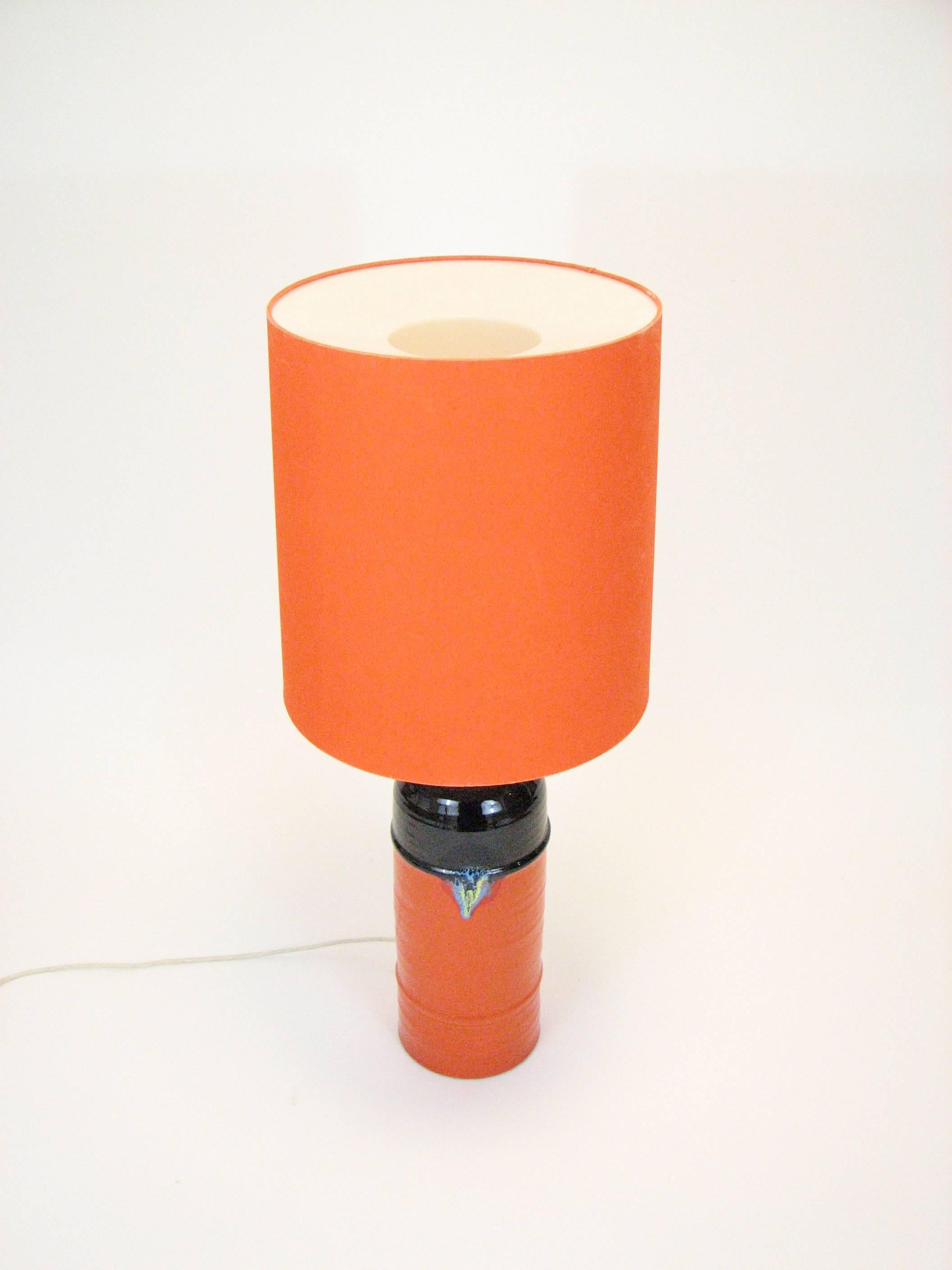 An extremely rare large-scale glazed and signed table lamp with original shade by Danish designer Bjorn Wiinblad for Rosenthal GmbH of Germany. The lamp features a turqoise, yellow and red focal point on an orange and black ceramic base, and a