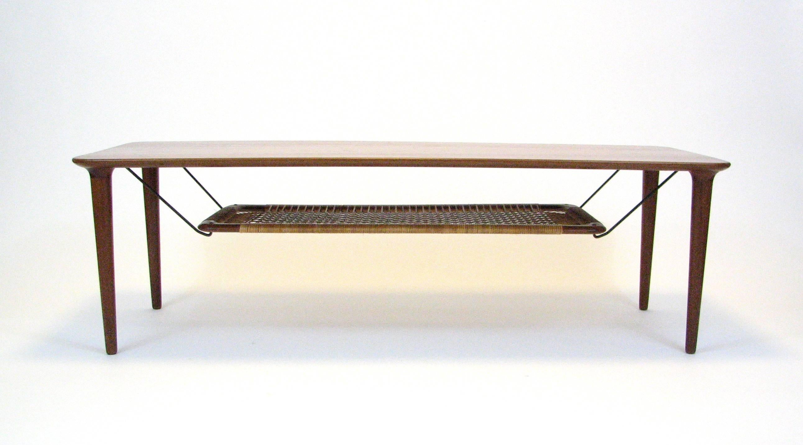 Mid-Century teak coffee table with cane magazine shelf by Gustav Bahus of Norway.  1960s.

In the manner of Peter Hvidt & Orla Mølgaard.

Well-preserved overall condition. One broken strand of webbing, as pictured.

Please note:  Pick up for this