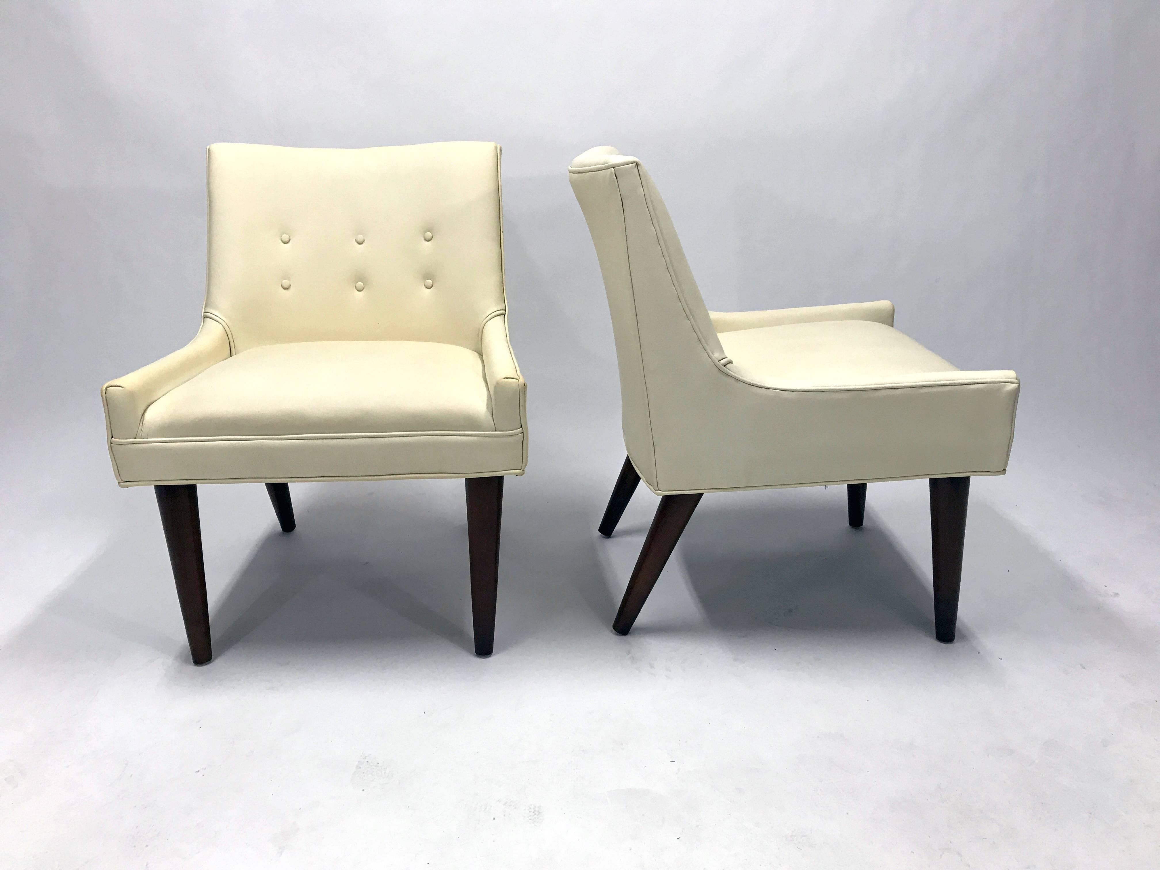 A pair of Mid-Century slipper chairs in the manner of Milo Baughman, a la his Model 176 chair produced by Thayer Coggin in the late 1950s.

In original ivory vinyl upholstery with walnut legs.

These chairs are located in Denver, Colorado.