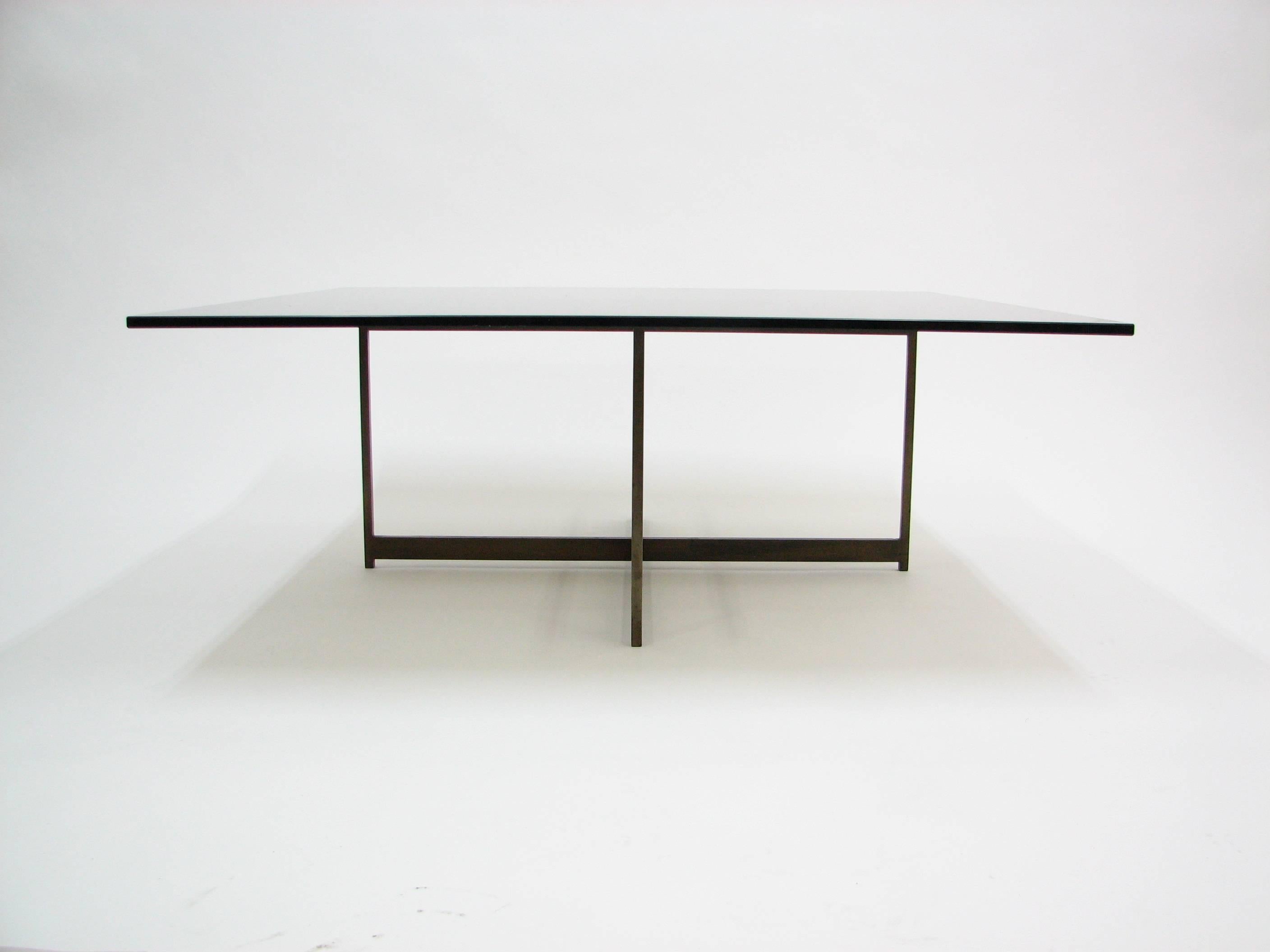 A beautiful Mid-Century smoked glass and bronze x-base coffee table in the manner of Milo Baughman. The weight of the base ensures stability and lack of movement. The glass has a flat polished edge and is 3/4