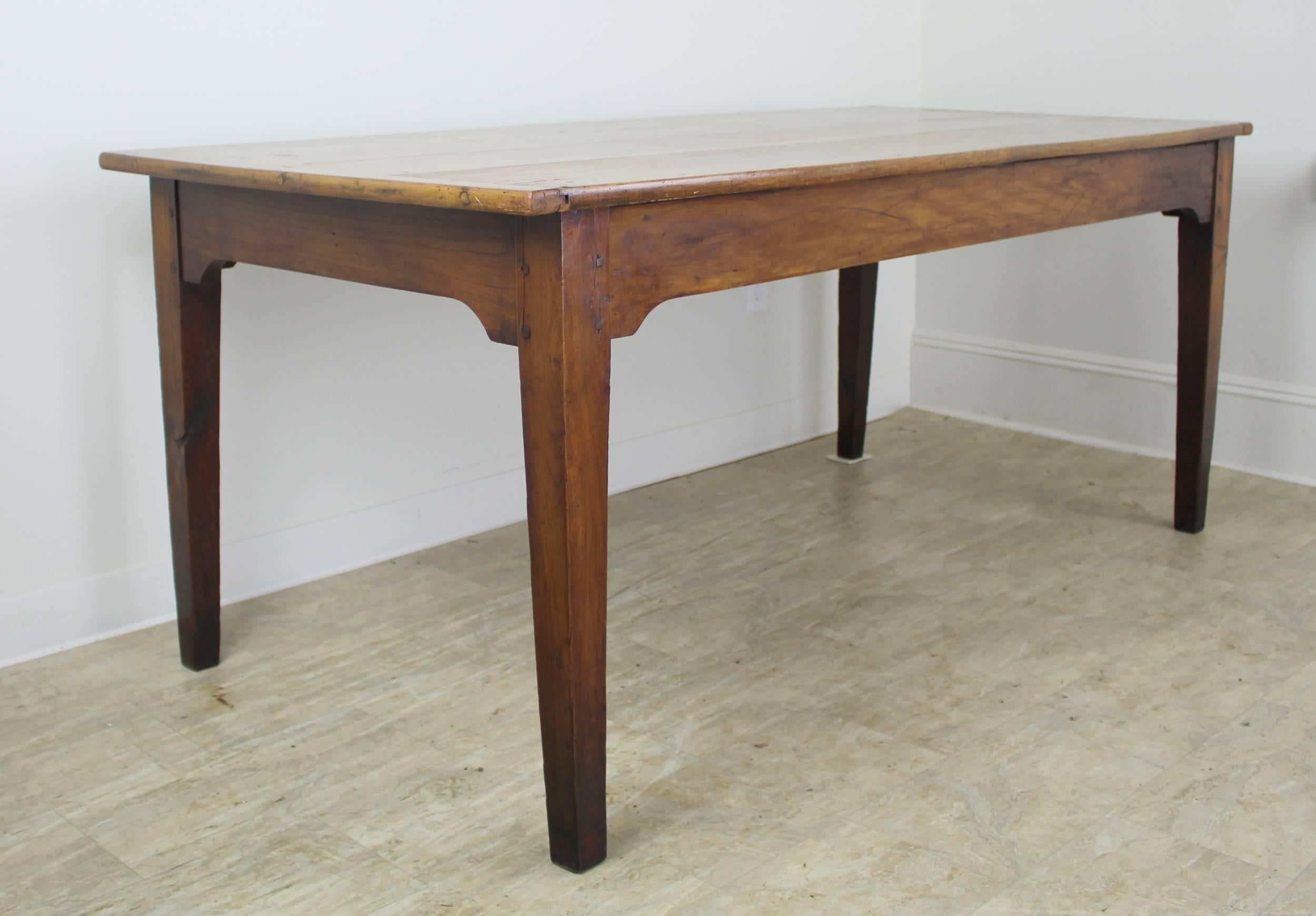A generously deep farm table with small breadboard ends in pale cherry, polished to a glow. Lovely patina. With 63.5 inches between the legs on the long side, this table can accommodate eight diners. Traditional tapered legs and shaped apron
